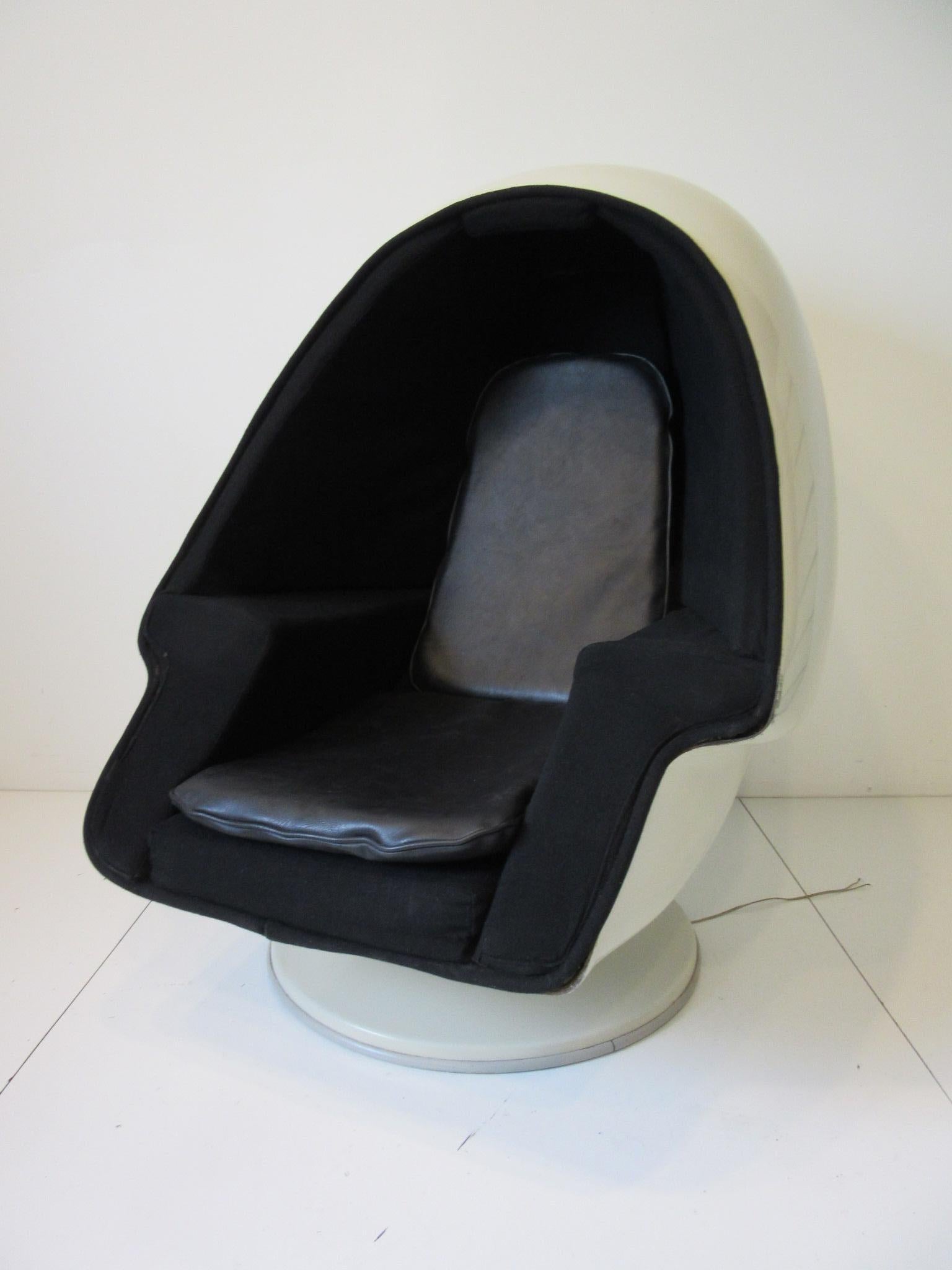 A white fiberglass egg styled chair with matching ottoman having stereo speakers to each inside panel sitting on a round base. The interior is upholstered in the original woven black contract fabric thru out with arm rests and additional