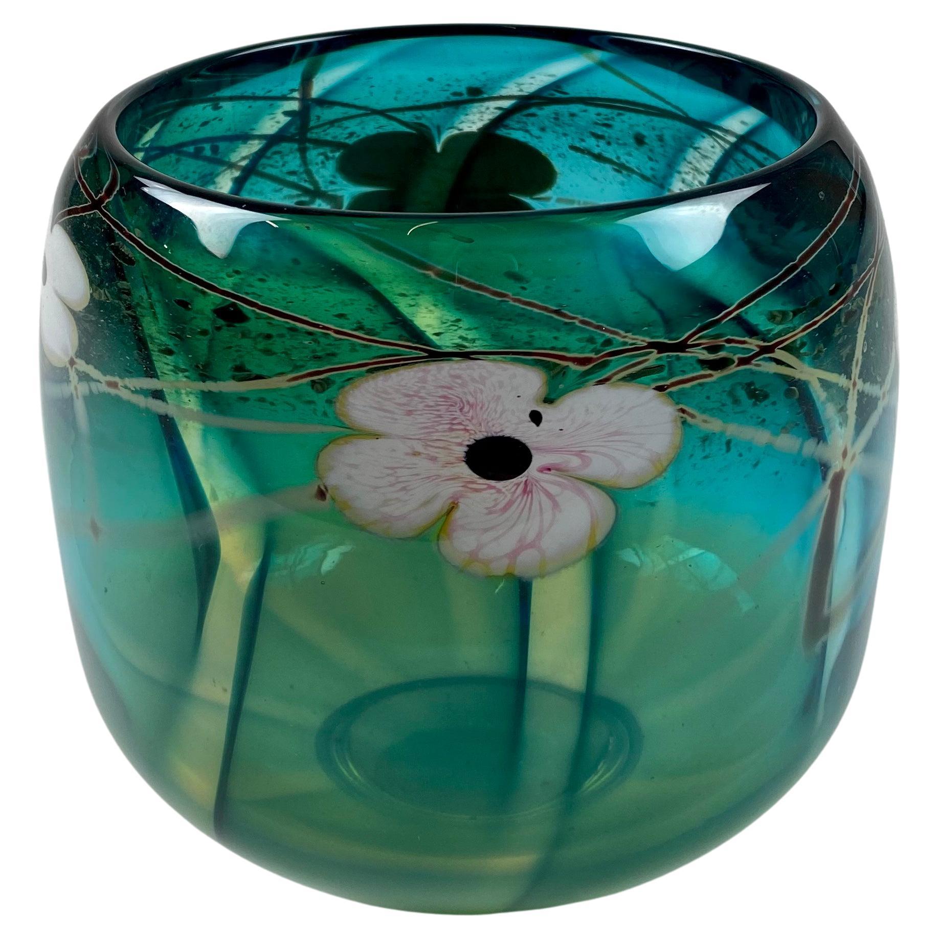 An Art Nouveau Art Deco style original David Nichols blown cased studio art glass vessel featuring white and pink dogwood blossoms in a teal ground, polished pontil. Signed at the underside. North Carolina.
