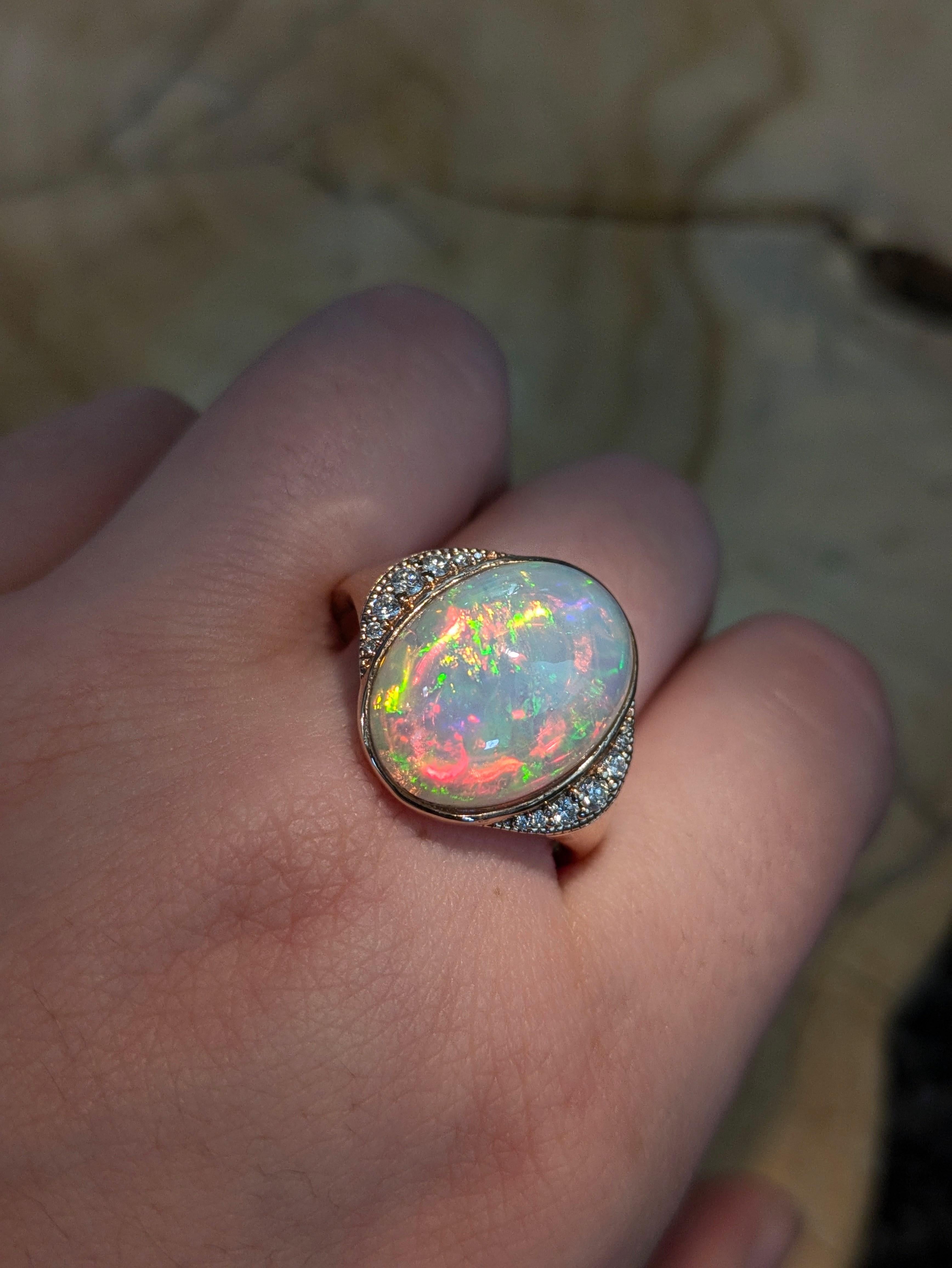 Este cautivador anillo presenta un luminoso ópalo etíope oval de 7,11 ct (16,8x13,2 mm), célebre por su vívido juego de colores. Engastado en oro de 14 quilates (4,31 g), el ópalo está acentuado por 14 brillantes diamantes que suman un total de 0,19