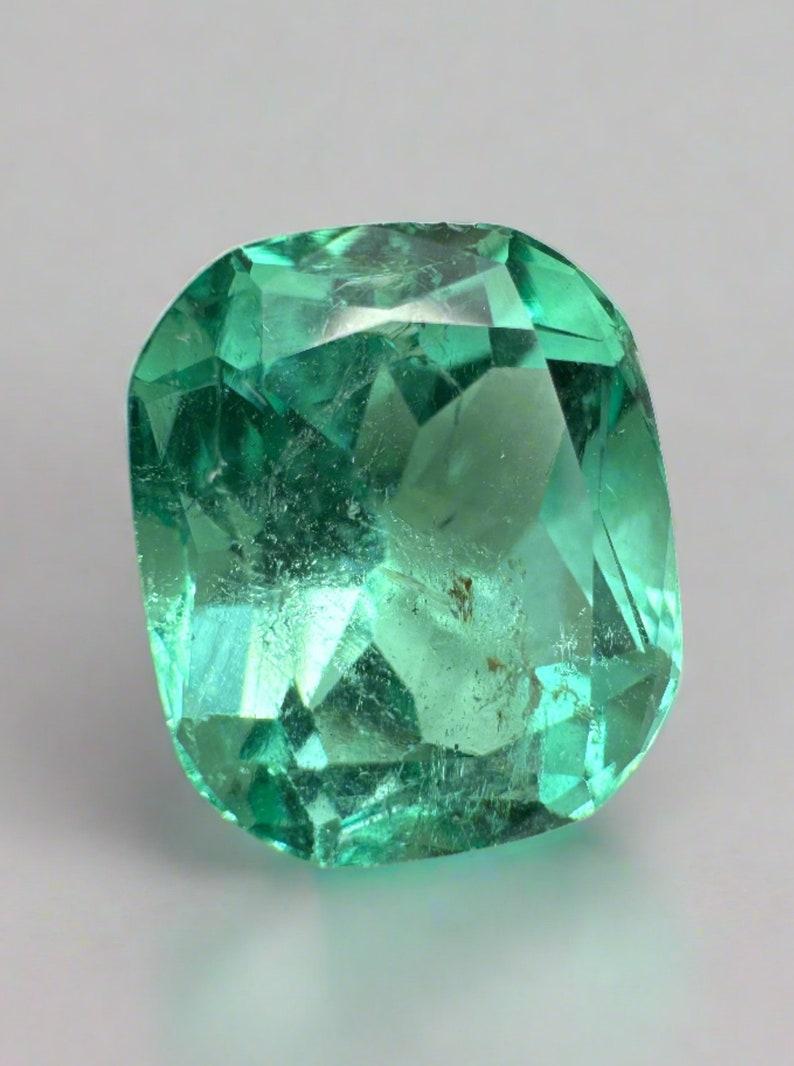 Stone: Emerald
Weight: 7.13-carats
Shape: Cushion Cut
Clarity: Transparent
Luster: Excellent
Color: Bluish Green
Measurements: 12.68mm x 10.86mm x 8.56mm
Geographic Origin: Colombia
Treatment: Natural, Oiling

Comments: Due to their growth
