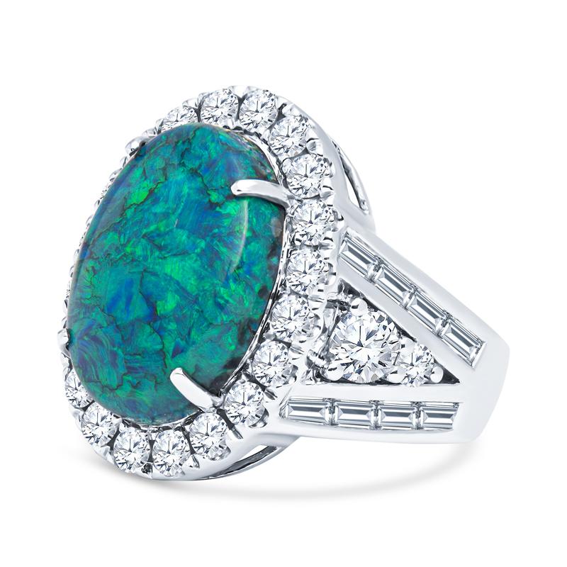 This spectacular Lightening Ridge Black Opal and Diamond ring features a 7.14 carat total weight black opal center with a phenomenal  blue and green play of color surrounded by a diamond halo featuring 2.59ct total weight in baguette and round
