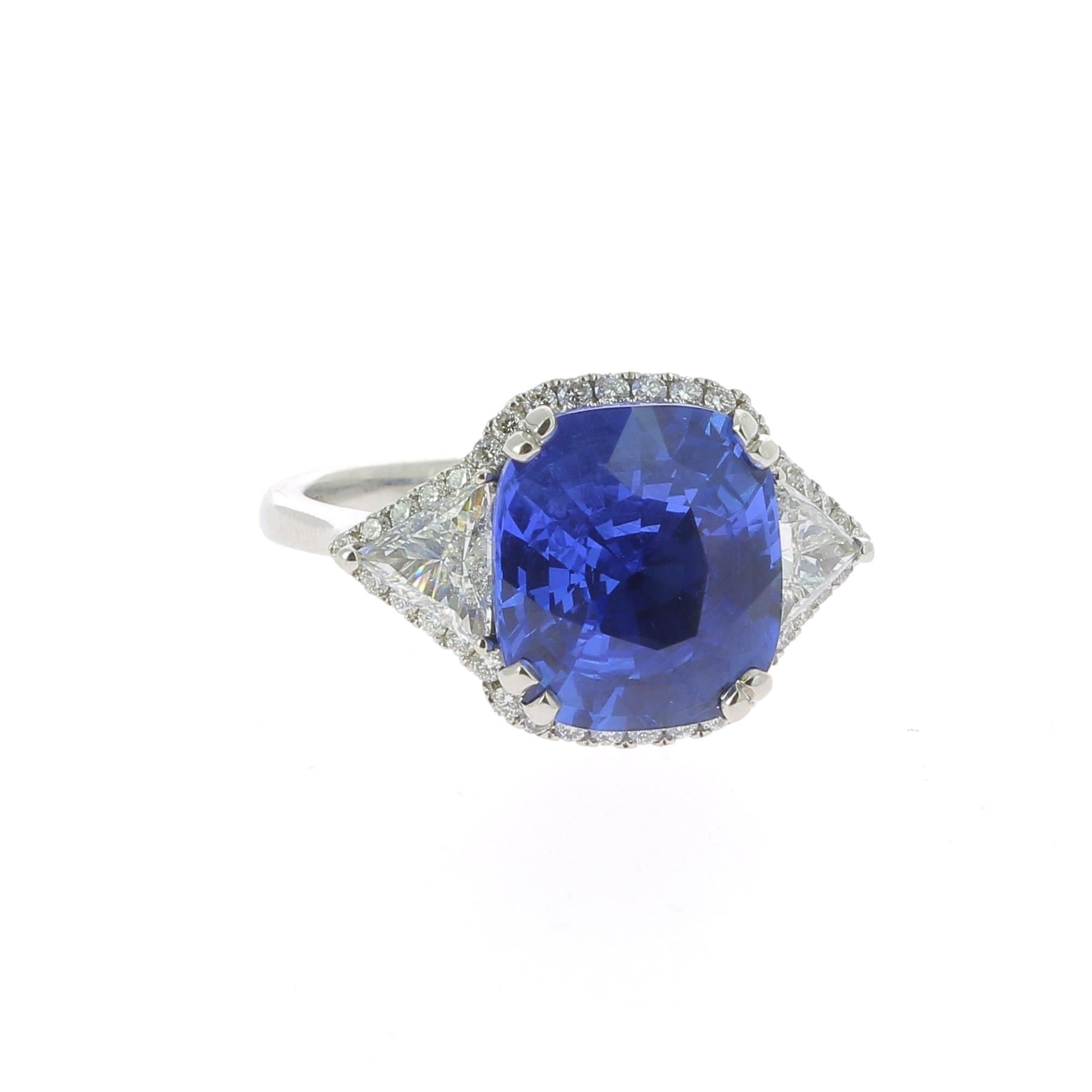 A Large and an amazing Cushion Blue Sapphire Ring, flanked on each side by a single triangle Diamond and surround by a halo of Diamond weighing 0.32 Carats.
The total weight of the Sapphire is 7.16 Carats, the gemstone is certified as an Intense