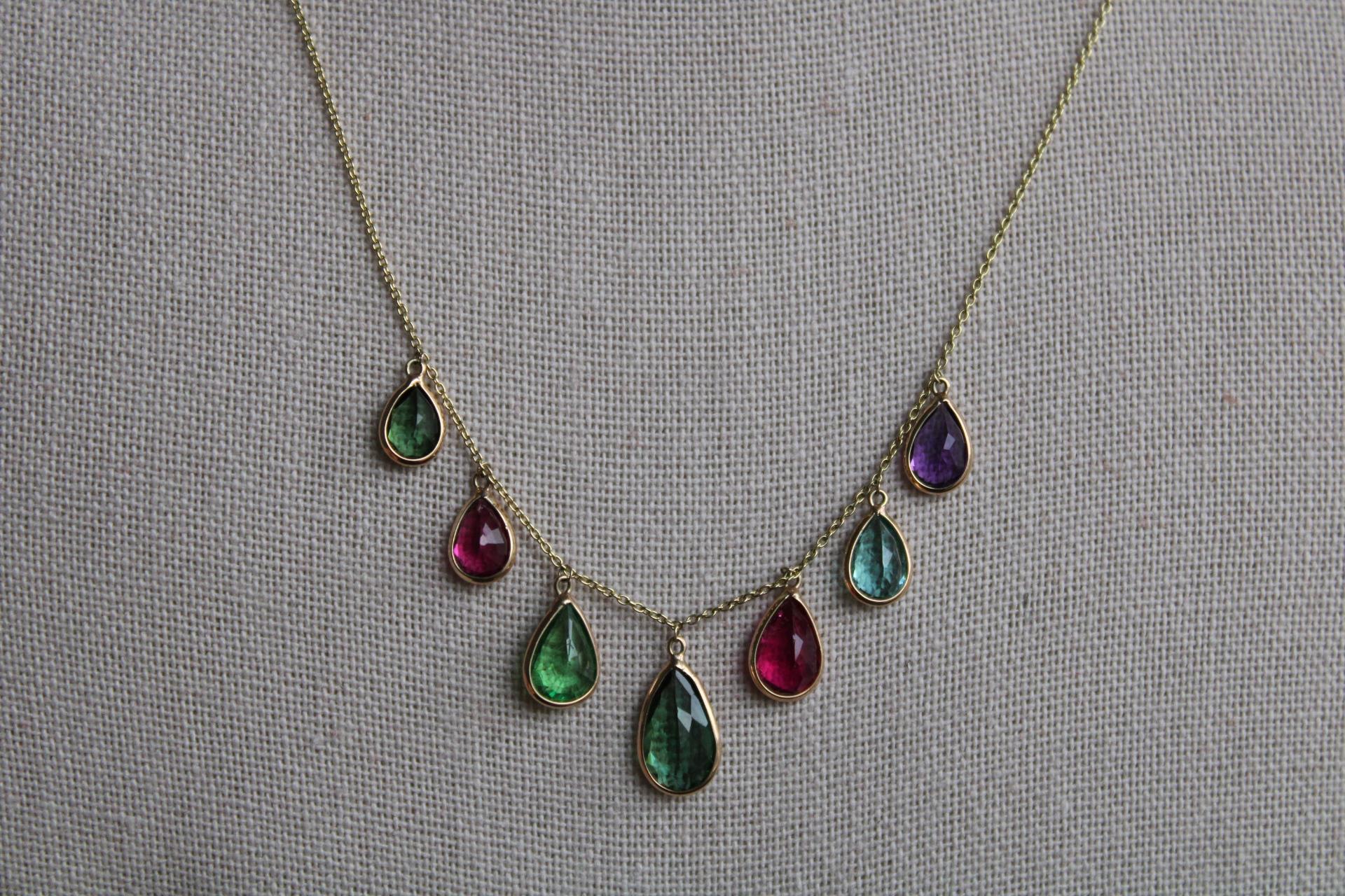 This beautiful multicolor stone 14K gold necklace is comprise of 7 pears. The center stone in a dark hunter green tourmaline, there are 2 lighter sage green tourmalines as well as 2 pink tourmalines. The necklace features 1 amethyst and 1 aquamarine