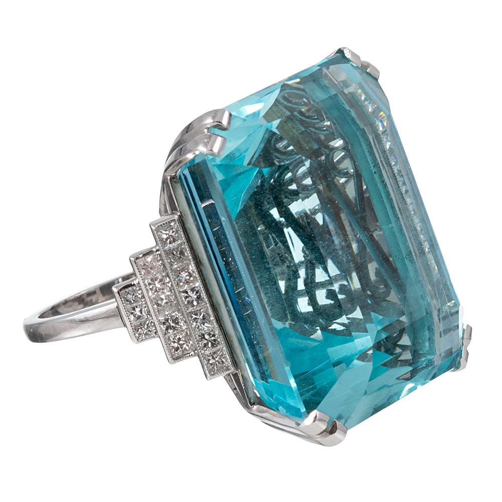 A striking ring of impressive size, the platinum mounting contains a 72 carat aquamarine flanked by three rows of stepped princess cut diamond accents. The diamonds weigh 1.12 carats in total and exhibit G-H color with Vs1-2 clarity. Note the styled