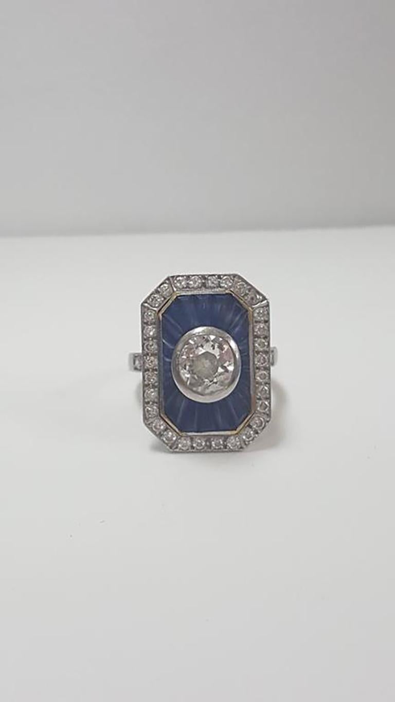 A lady’s diamond and sapphire cocktail ring, set in a platinum mounting. Edwardian, art deco transitional style circa 1915-1920.
Featuring a center bezel set Old mine cut diamond surrounded by a rectangular yellow gold bezel frame containing channel