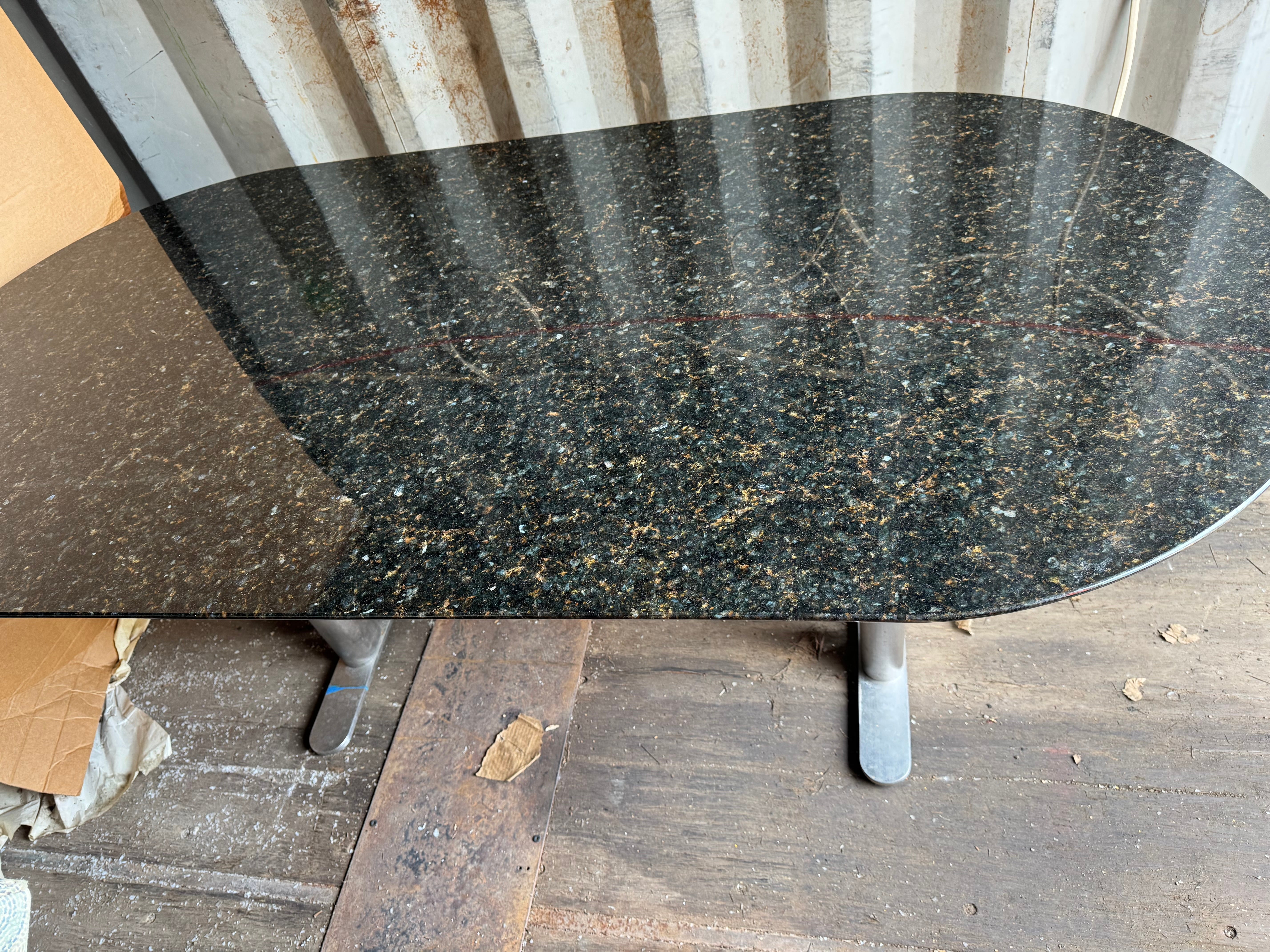 Il s'agit d'une table de salle à manger moderne John Geiger en forme d'hippodrome, avec une base en acier inoxydable et un plateau en granit.
Le sommet est en forme d'hippodrome. La base est composée de 4 pieds reliés à une barre d'acier qui