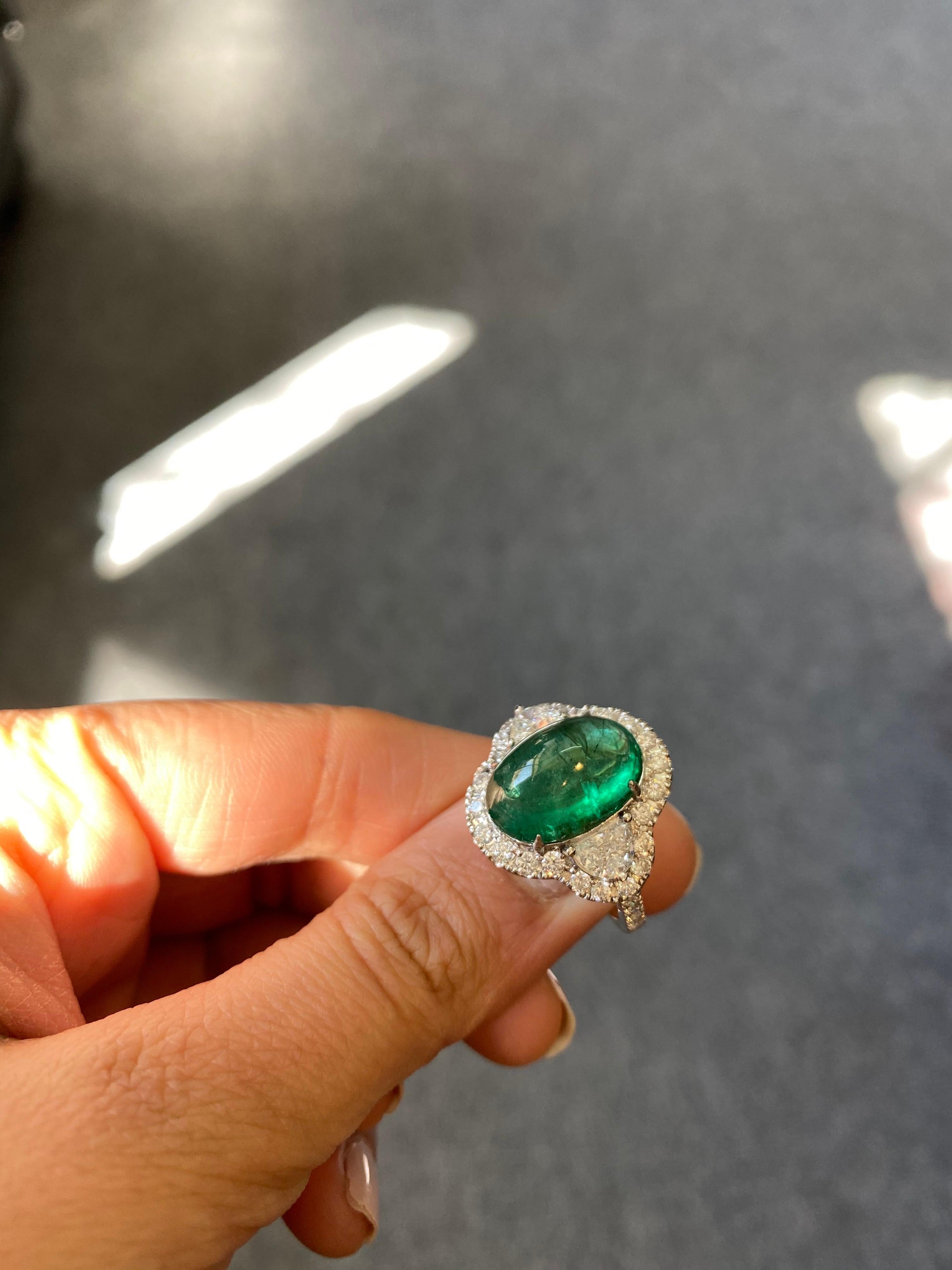 A stunning three-stone engagement ring, with a 7.25 carat transparent Zambian Emerald cabochon centre stone and 2 half-moon side stone diamonds (totalling 0.81 carats), with a diamond halo all set in 18K white gold. Currently a ring size US 6, but
