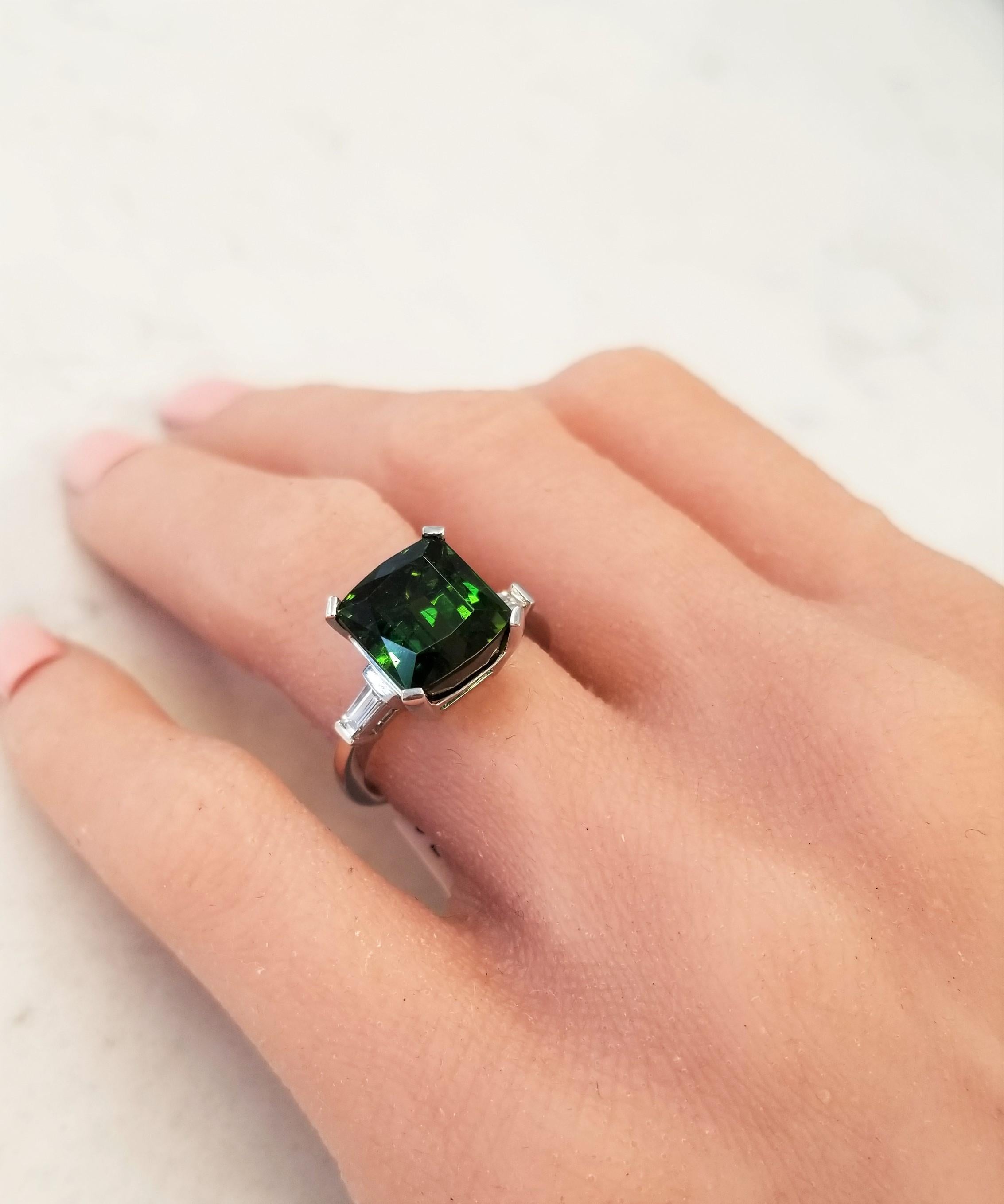 This is a 7.28 carat green tourmaline with impeccable cutting and shape, designed to highlight each expertly placed facet in a classic 3-stone ring. Its gem source is Brazil; its color is forest green with superb transparency and clarity. It