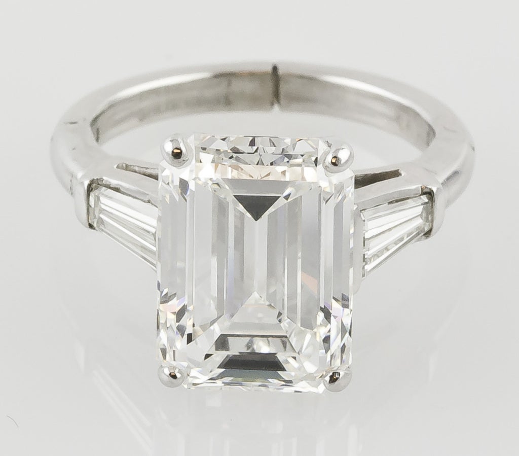 Very fine platinum and emerald cut diamond engagement ring. It features a GIA certified 7.29cts H color VVS1 clarity diamond featuring Very Good polish, Very Good symmetry, and faint florescence. Also features approx. 0.80cts of tapered baguette-cut