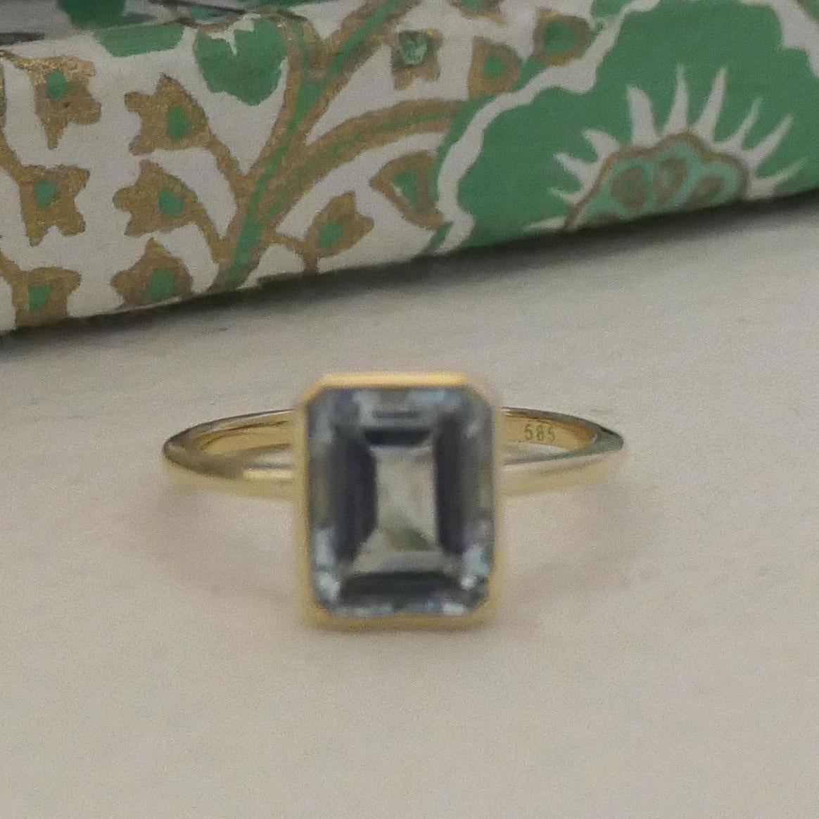 This elegant ring features a captivating 7.2x9mm aquamarine gemstone set in a sleek 14kt yellow gold bezel setting. The soft, pale blue hue of the aquamarine contrasts beautifully with the warm golden tones, creating a timeless and refined look. The