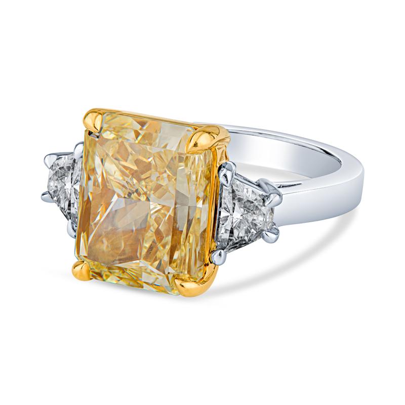 This beautiful engagement ring features a 7.32 carat radiant cut fancy yellow diamond cradled in 18 karat yellow gold. The center is flanked by 0.70 carat total weight in two trapezoid cut diamonds set in platinum. This ring is a size 6.5 but can be