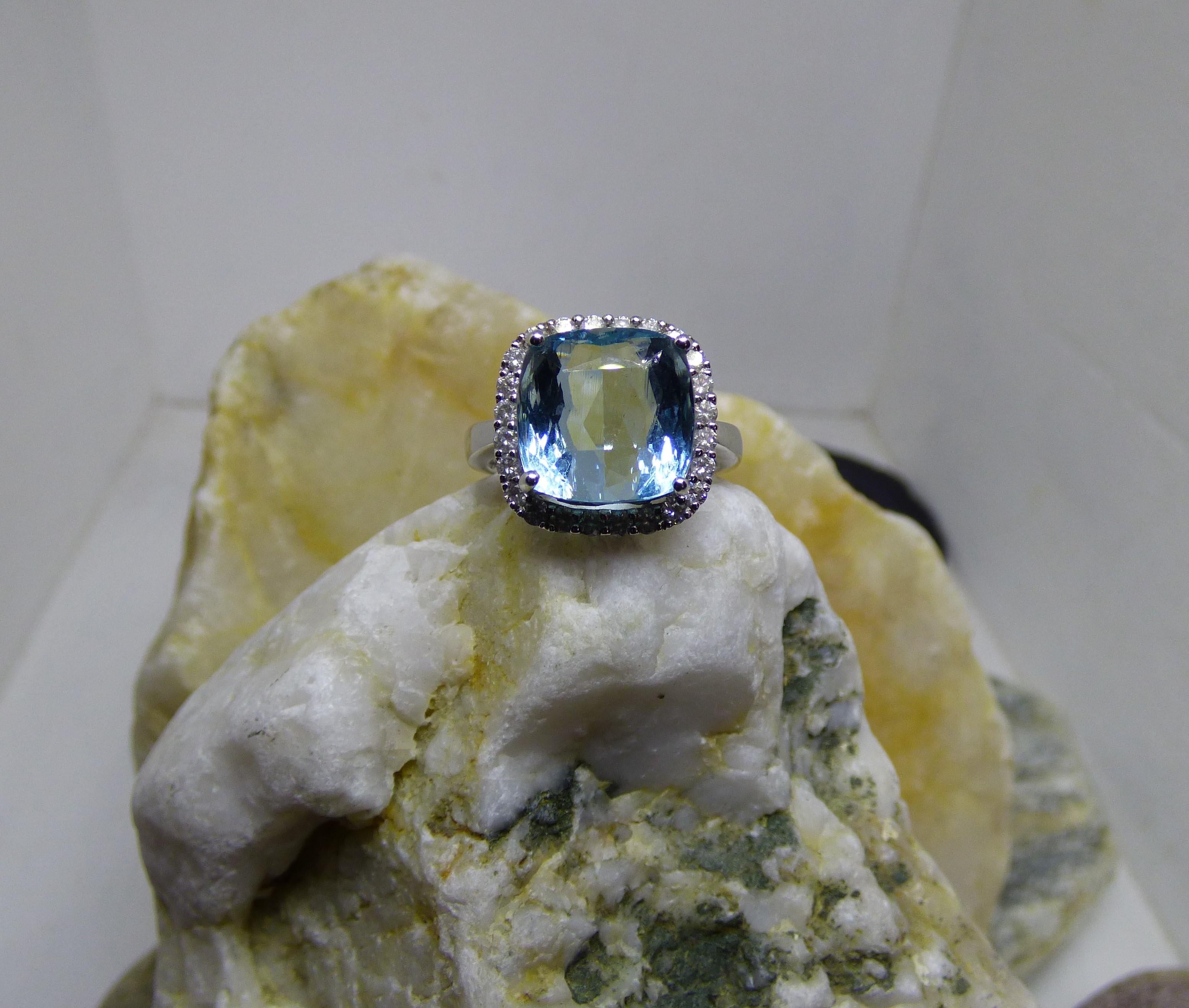 A bright Aquamarine cushion cut stone is surrounded by Diamonds in this ring. The Aquamarine is 12X12mm and 7.32ct. It is surrounded by 24 Diamonds with a total Diamond weight of .55ct.  The ring is handmade in 18K white gold and hallmarked by the