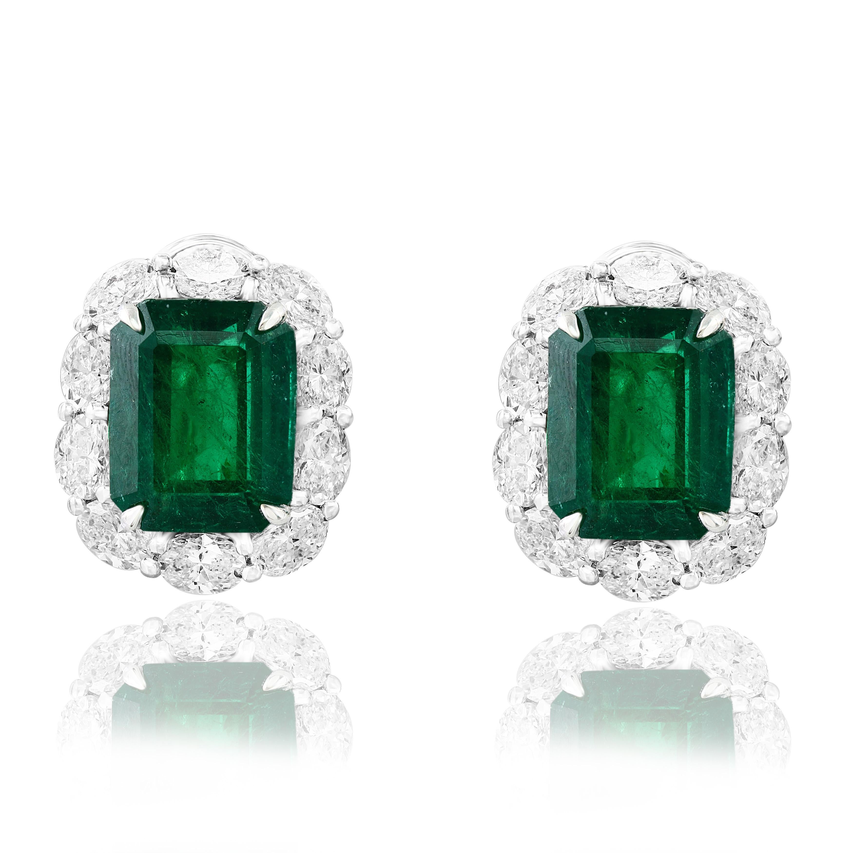 Showcasing two color-rich Emerald cut Lush Green Emeralds weighing 7.44 carats total, surrounded by a single row of oval-cut brilliant diamonds. 20 Accent diamonds weigh 2.89 carats in total. Set in 18 karats white gold. Omega Clip with the
