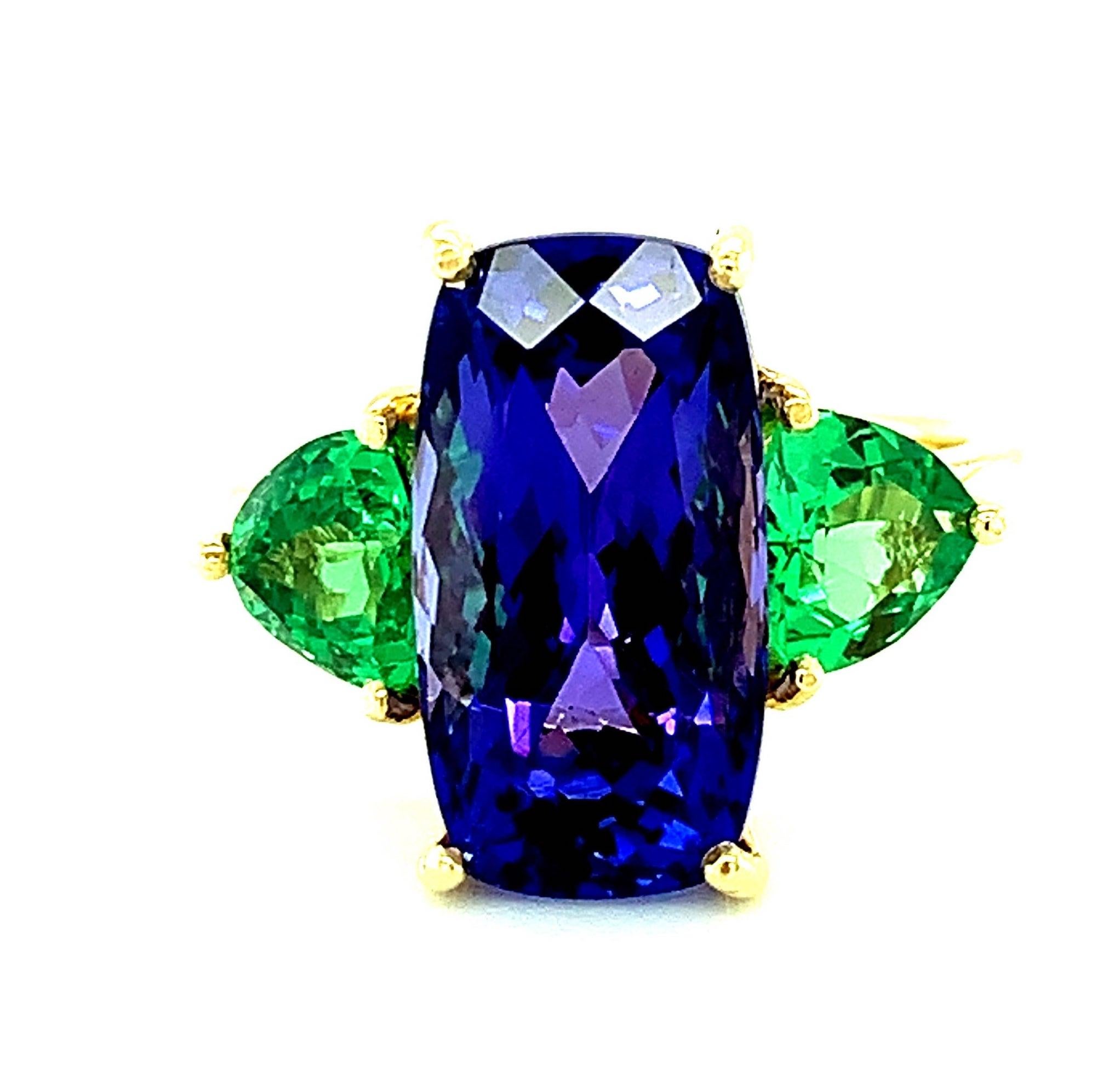 This stunning ring features a large, 7.44 carat cushion-shaped tanzanite and trillant-cut tsavorite garnets, all with spectacular color! The tanzanite has intense color and shows flashes of both blue and purple separately, which is a unique look,