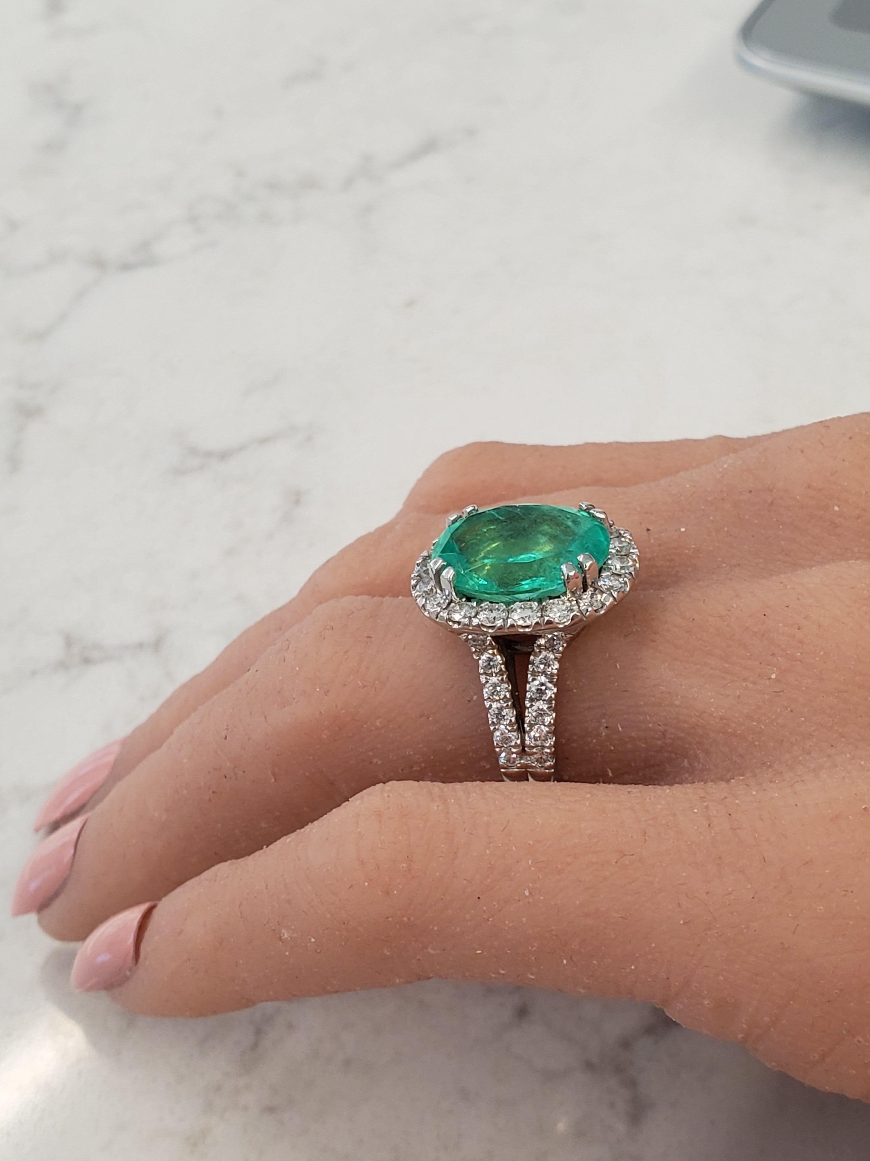 This is a 7.50 carat oval cut green emerald. It measures 15.00-12.22mm. The gem source is Brazil; its color is green combined with slight yellow undertones. A total of 42 scintillating round brilliant cut diamonds are prong set and arranged in a