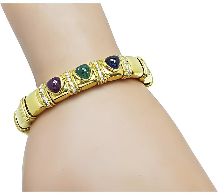 Dies ist ein charmanter Armreif aus 18k Gelbgold. Der Armreif ist mit einem schönen Cabochon in Herzform aus Smaragd, Rubin und Saphir mit einem Gewicht von etwa 7,50 ct besetzt. Die Farbsteine werden durch funkelnde Diamanten im Rundschliff mit