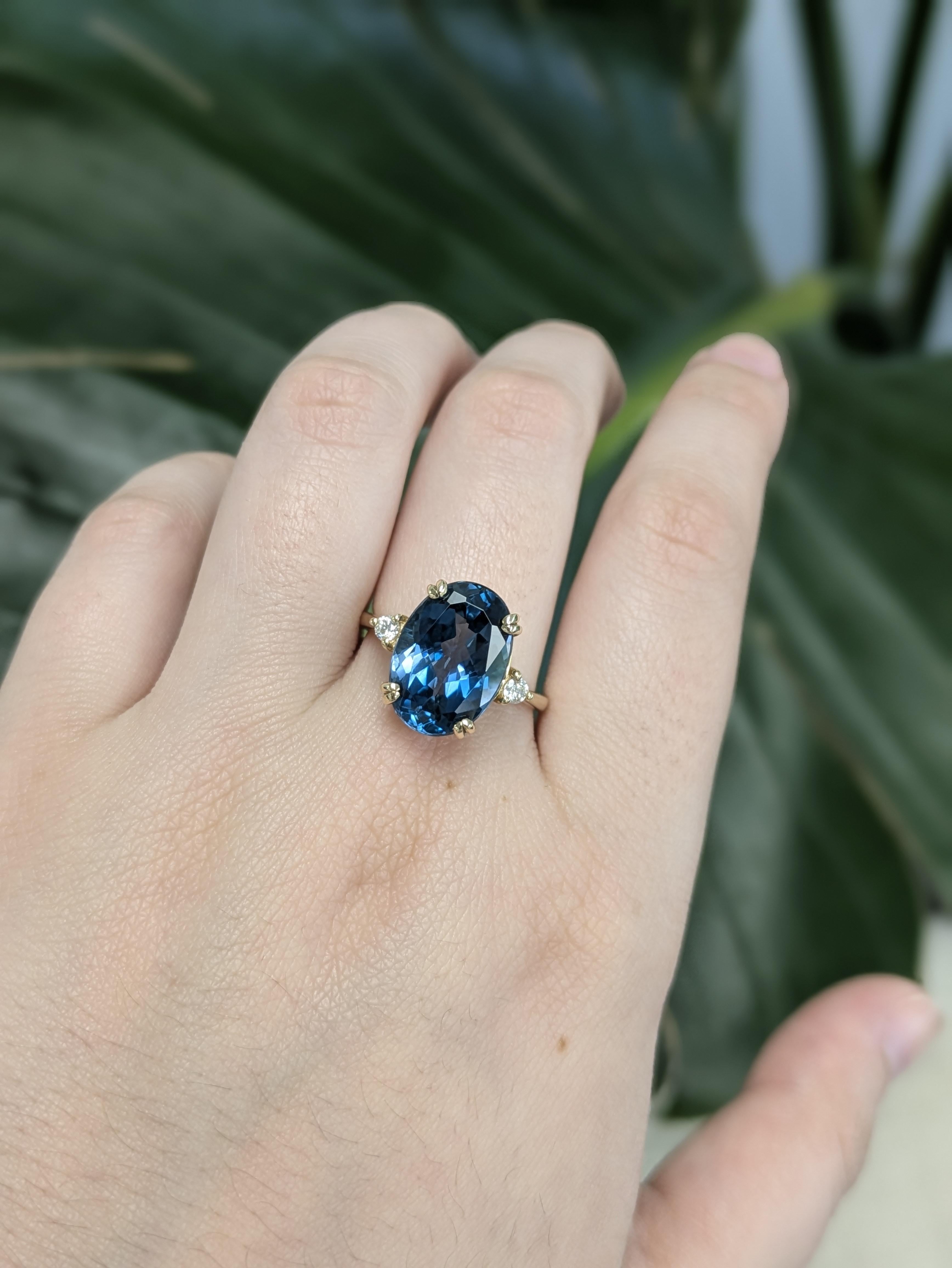 This exquisite ring features a stunning 7.55ct oval-shaped London Blue Topaz, measuring 14x10mm, treated by irradiation to enhance its deep, vivid hue. Set in 14k gold (3.08g), the center stone is accented by two sparkling diamonds totaling