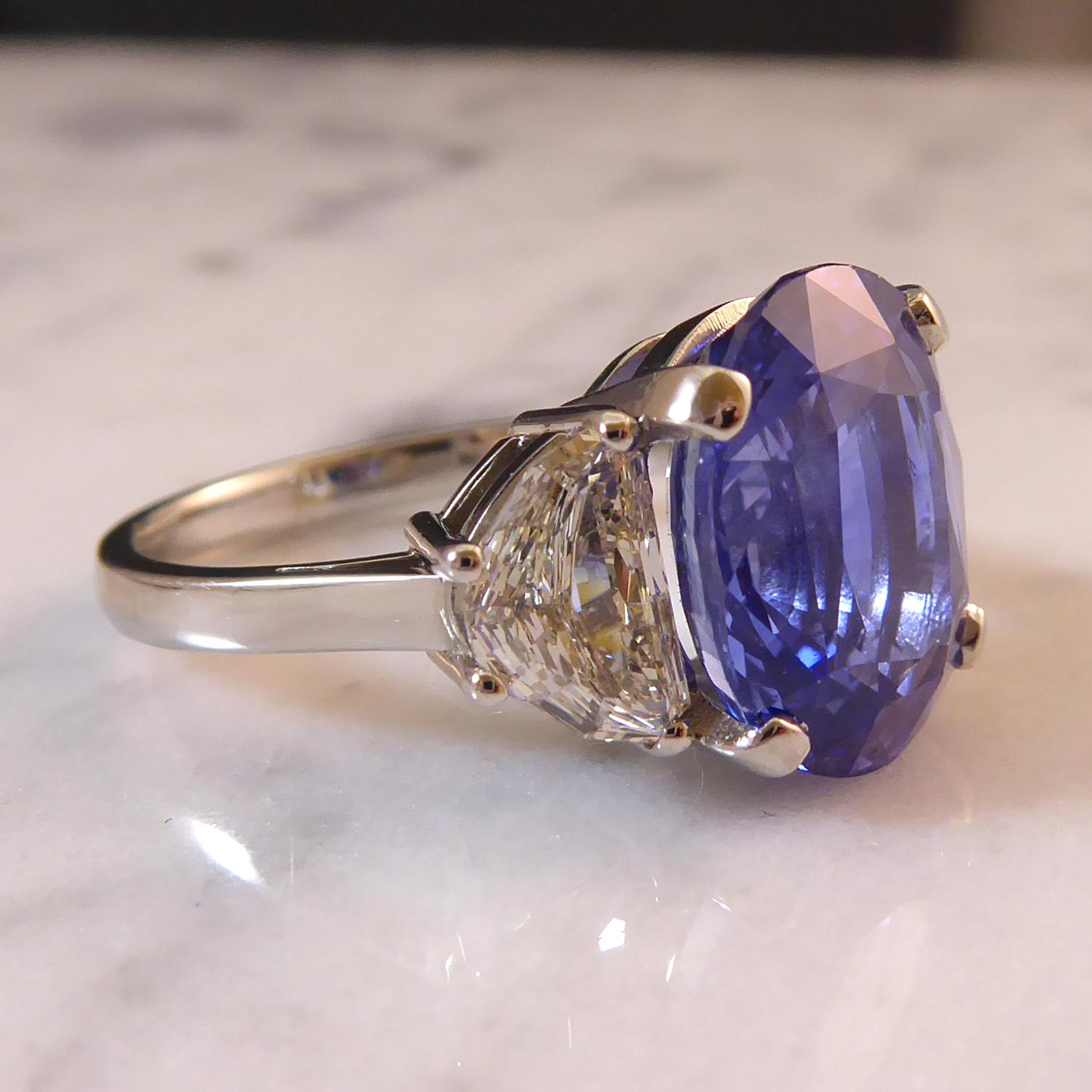 A standout 7.58ct  oval mixed cut sapphire and half-moon diamond three stone ring.  Centrally set with a pale blue sapphire measuring some 12.59mm x 10.17mm x 6.43mm deep with only light to moderate inclusions and showing some colour banding.  The