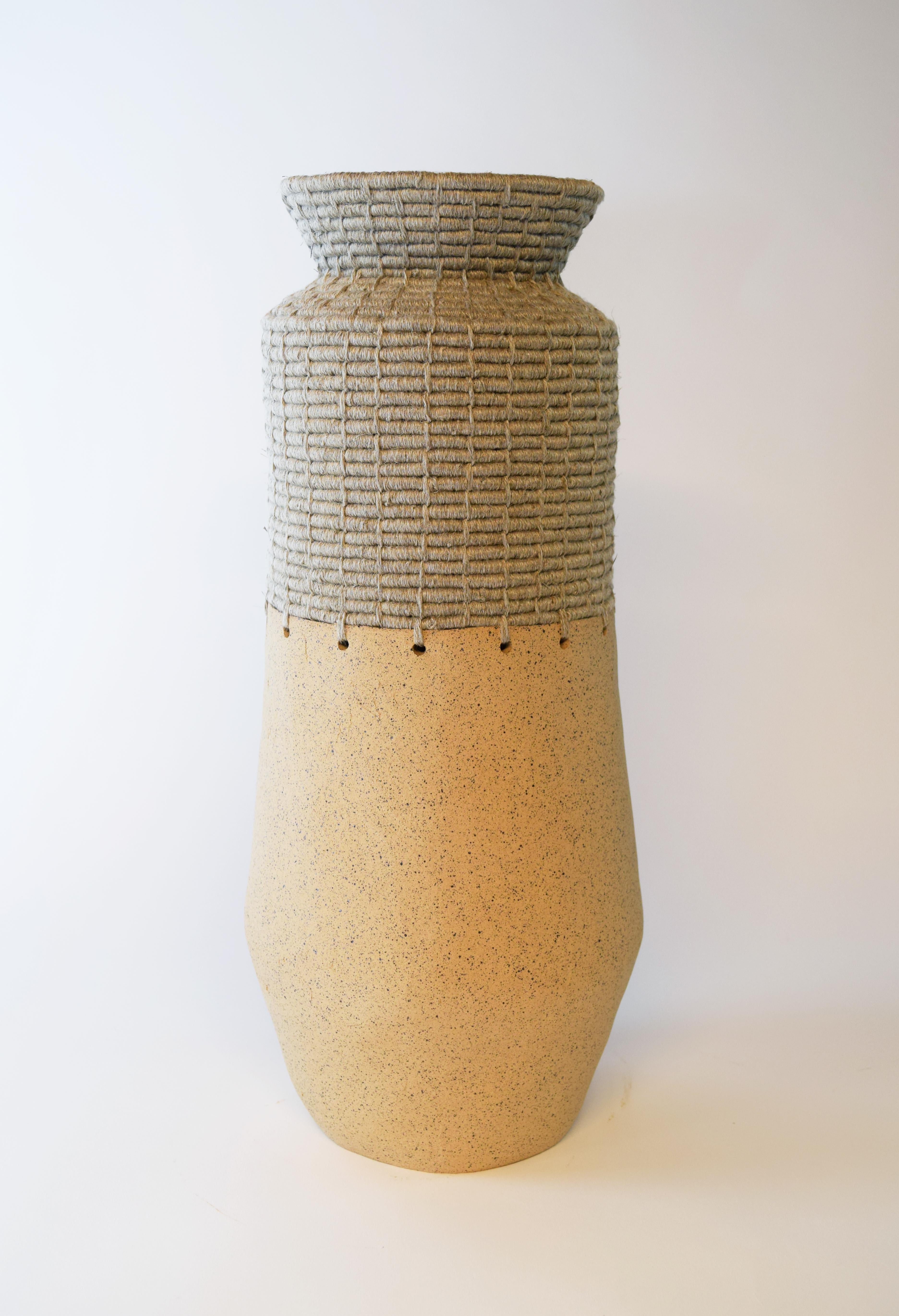 763 Natural vessel by Karen Gayle Tinney
Dimensions: D 18 x W 18 x H 44 cm 
Material: Unglazed speckled beige stoneware, natural undyed linen.

Karen Gayle Tinney is an artist and designer whose work consists of pieces that combine ceramic and