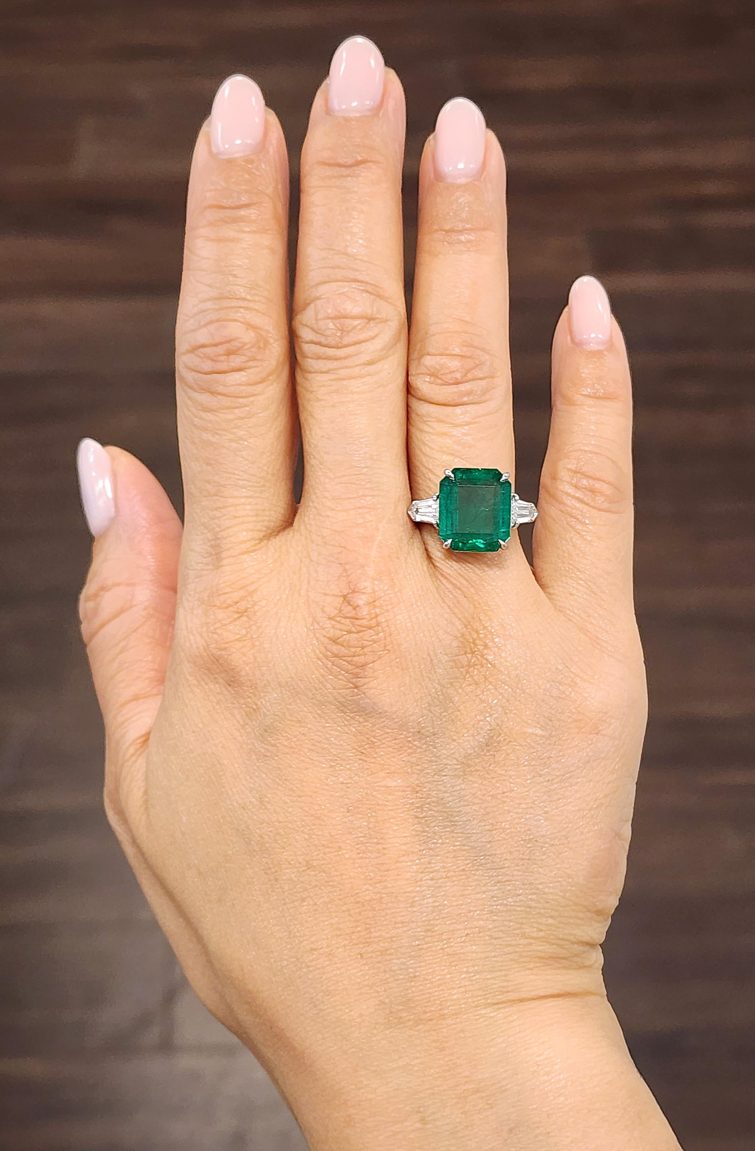 This striking cocktail ring showcases a 6.89-carat GIA certified emerald-cut emerald, radiating a vivid green hue. Flanking the centerpiece are two bullet-cut diamonds, totaling 0.75 carats, with a clarity of VS1/VS2 and a color grade of F/G. The