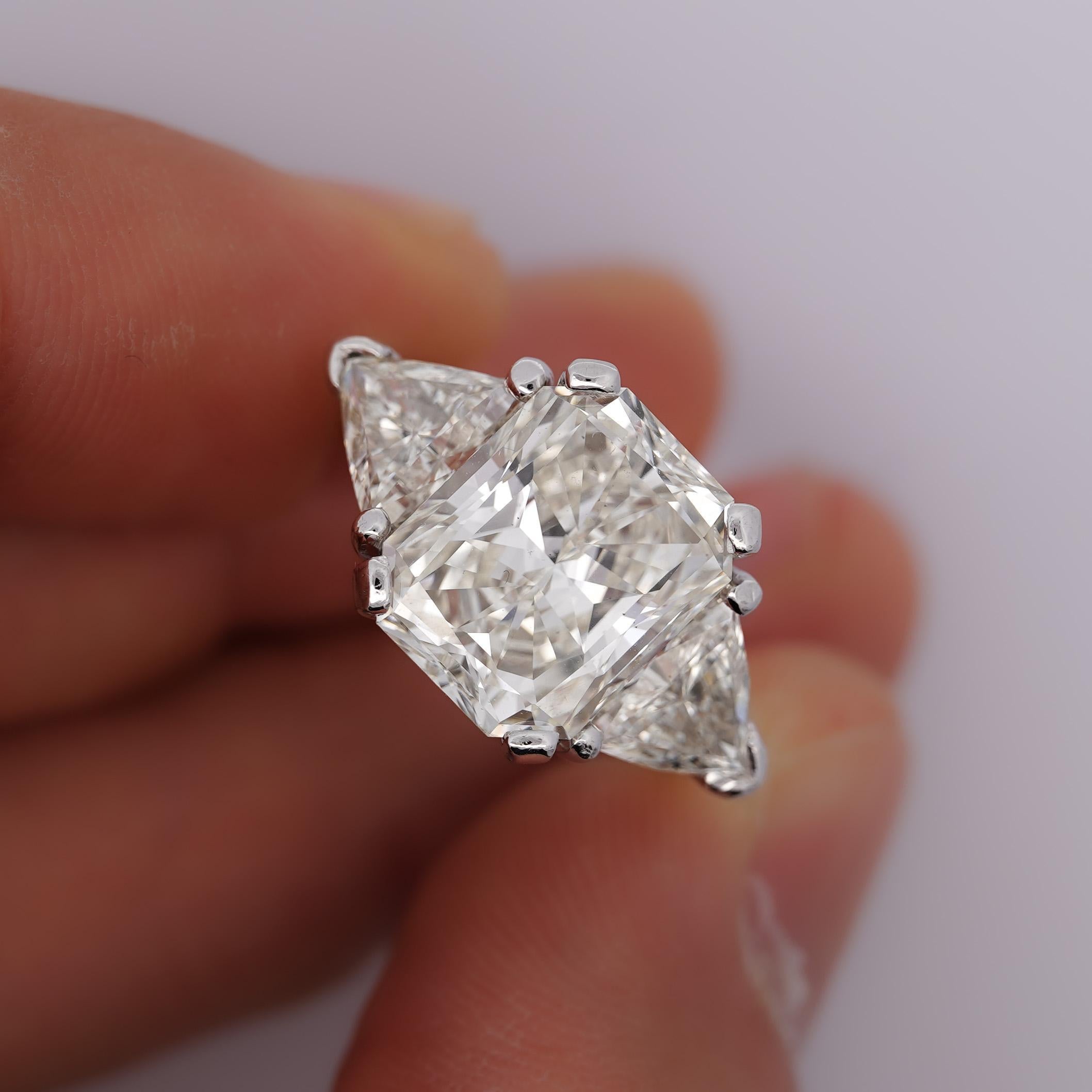 Natural 6.08 Carat Radiant Cut H/VS1 Diamond Three Stone Engagement Ring In Platinum. Set with 2 Trillion Cut Diamond Side Stones. Ring Size 6, adjustable.

Details: 
Item Type: Three Stone Engagement Ring
Metal:  Platinum
Ring Size: 6