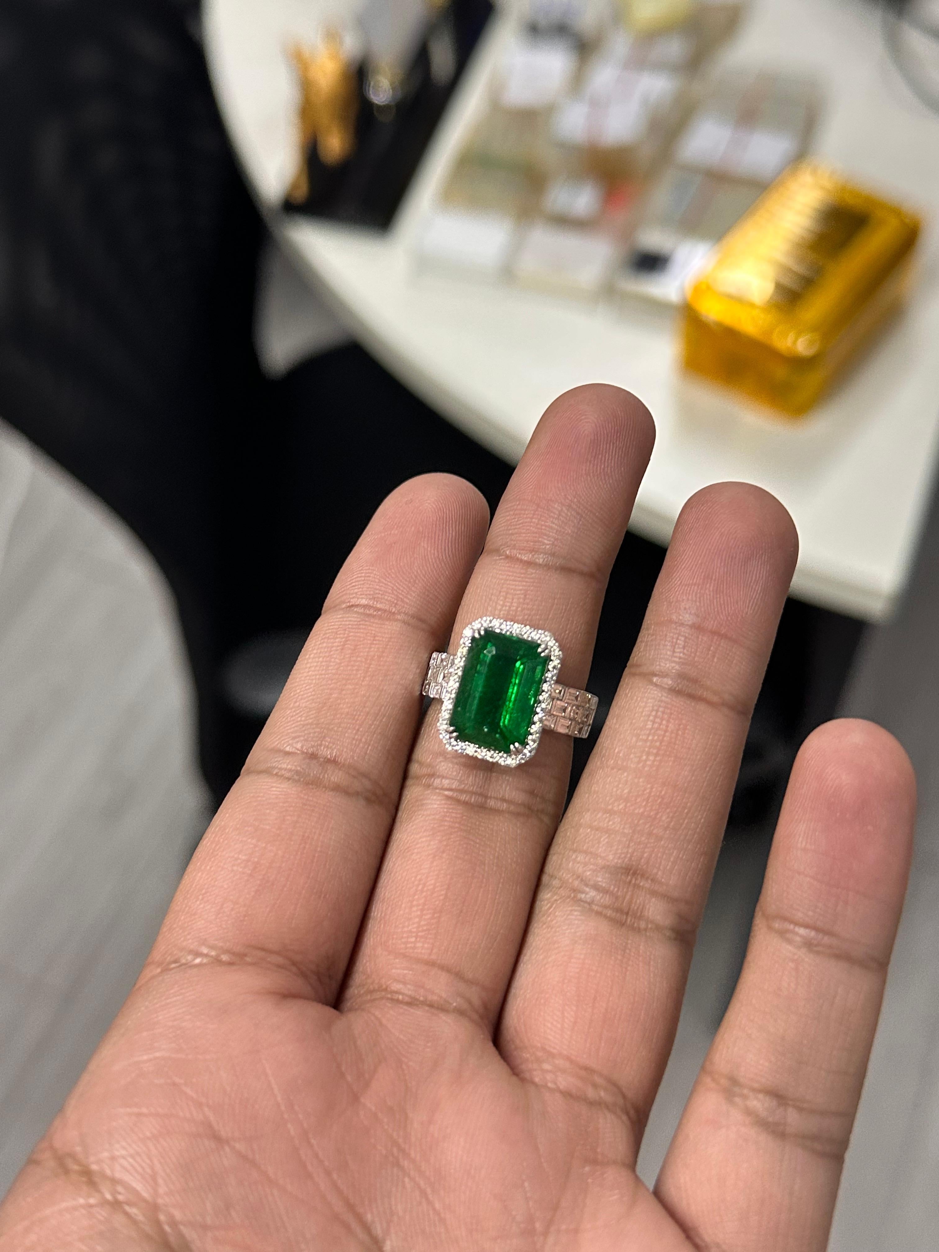 A captivating fusion of color and craftsmanship, this luxurious ring features a vivid 7.70 carat natural Zambian emerald, cut in a striking emerald shape that emphasizes its rich, saturated vivid green hue. This exceptional gem has undergone minor