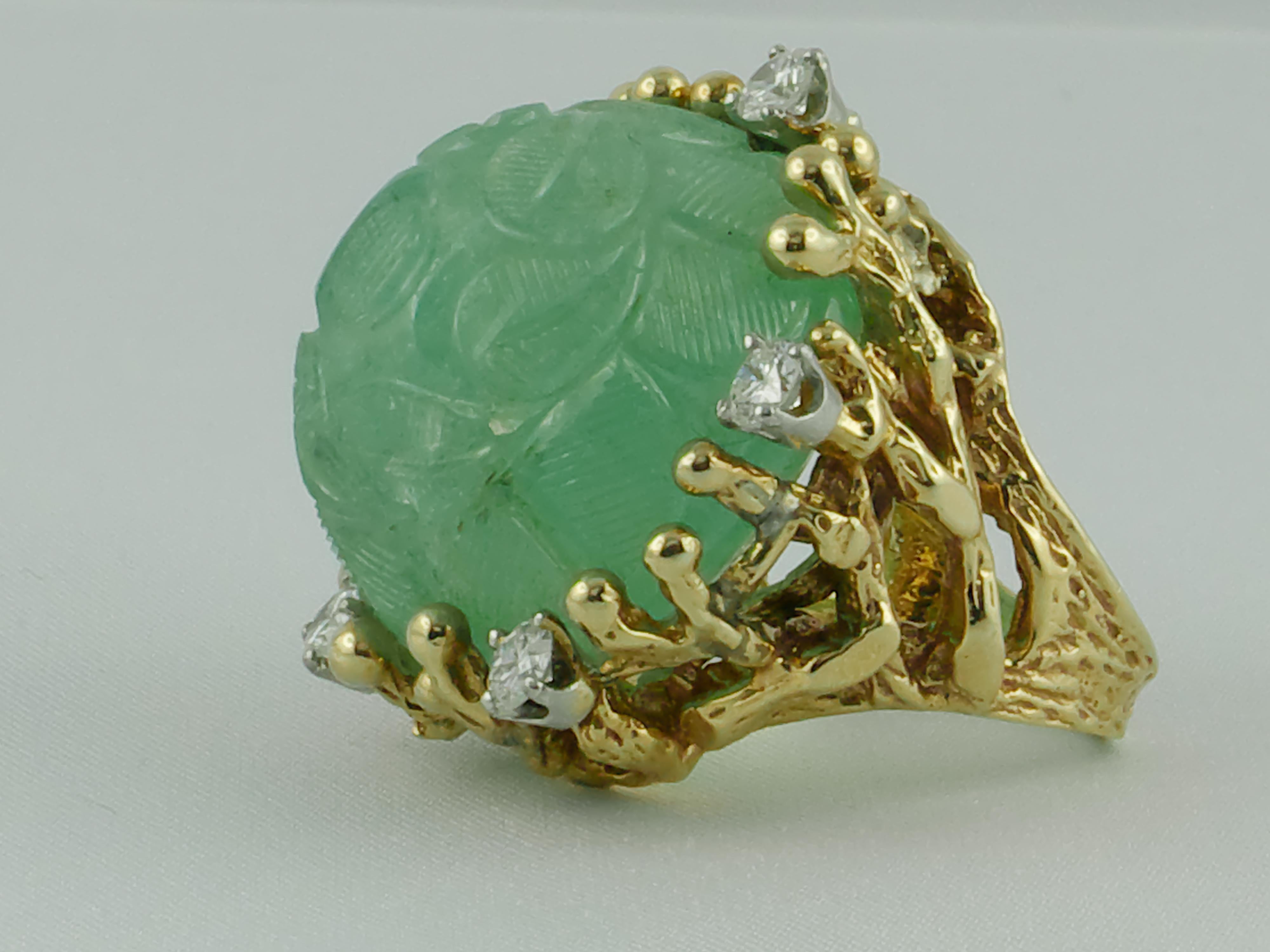 A stunning and imposing 1960s Cocktail Ring featuring a fabulous exquisitely carved 77.54 cts Emerald and 6 white round cut  Diamonds, approx 1.2cts,  set in an 18 karat Yellow Gold gnarled decor.
The shank is finely chiseled like a branch that