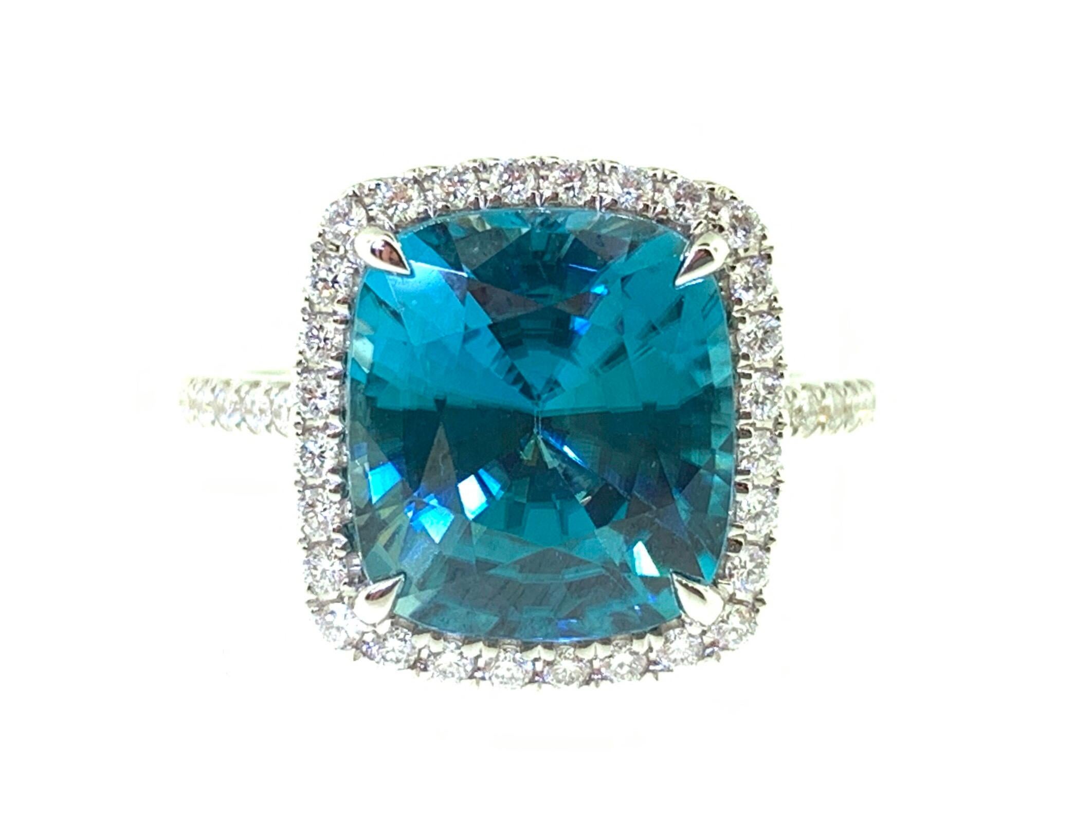 This stunning cocktail ring features a beautiful 7.76 Carat Cushion Blue Zircon with a Diamond Halo, on a Diamond Shank. This ring is set in 18k white gold, Ring Size is 6 1/2. Total Diamond Weight = 0.37 carats.