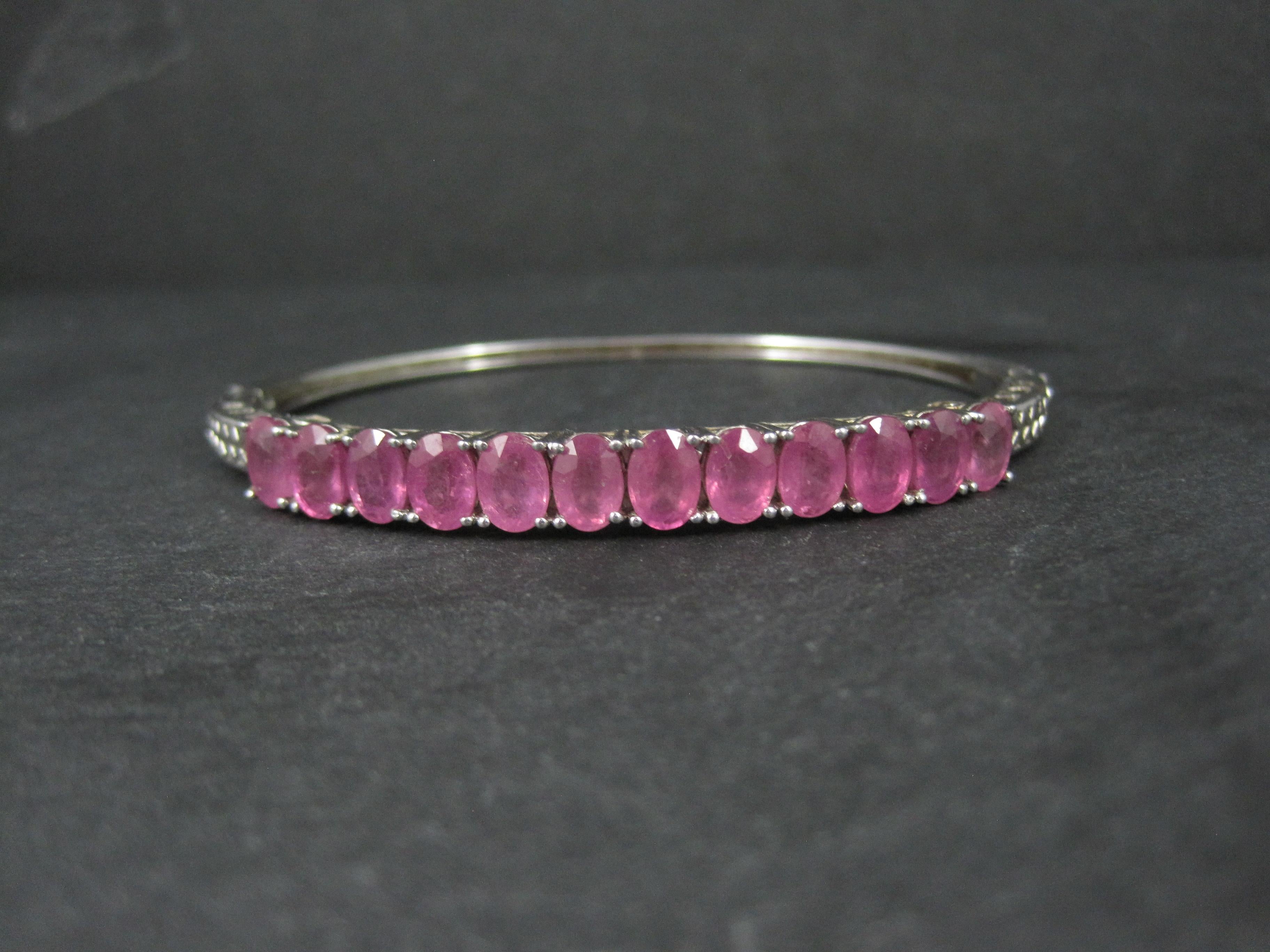 This gorgeous bangle bracelet is sterling silver.
It features 12 oval cut 5x7mm pink sapphire gemstones with an estimated total weight of 7.8 carats.
This bracelet measures 5/16 of an inch at its widest point. It has an inner diameter of 2 by 2 1/2