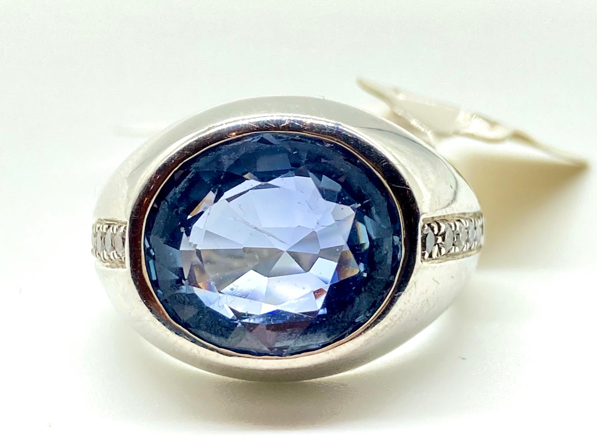 A beautiful white gold ring with an oval cut light blue Ceylon sapphire measuring 7.80 carats, bordered by 0.15 carats of round brilliant cut diamonds. Circa 1970. Certificate available.