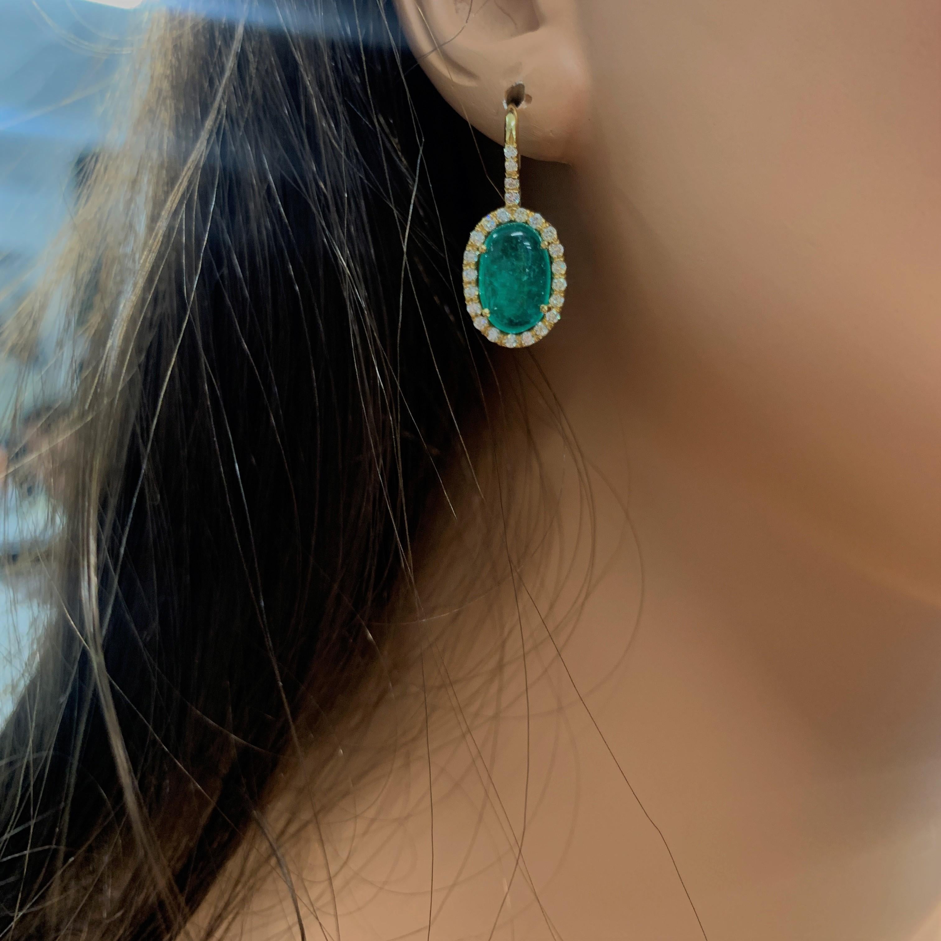 Allow these stunning emerald and diamond dangle earrings to entice you! These pretty, brightly polished 18k yellow gold drop earrings feature two oval cabochon cut intense green fine quality emeralds prong set in the middle, totaling 7.81 carats.