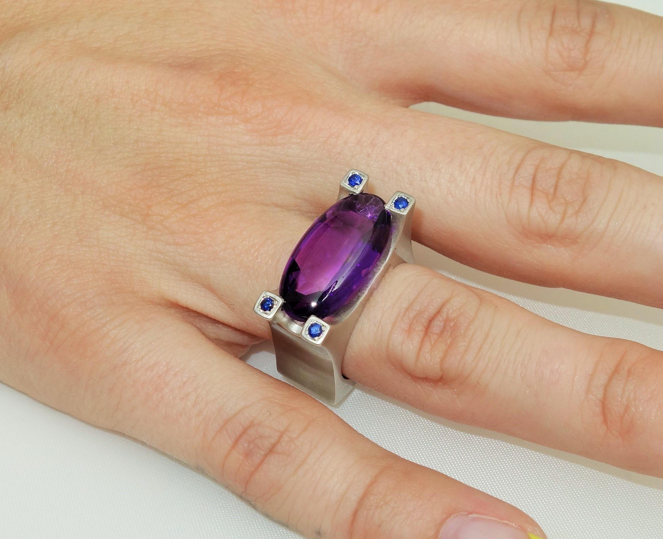 Stunning solitaire ring featuring a 7.85 carat oval facet-cut Amethyst; enhanced with a sapphire in each corner; 4 Sapphires approx. 0.12tctw; Sterling Silver Tarnish-resistant Rhodium Satin finish mounting; Size 7, we offer ring re-sizing. Stylish