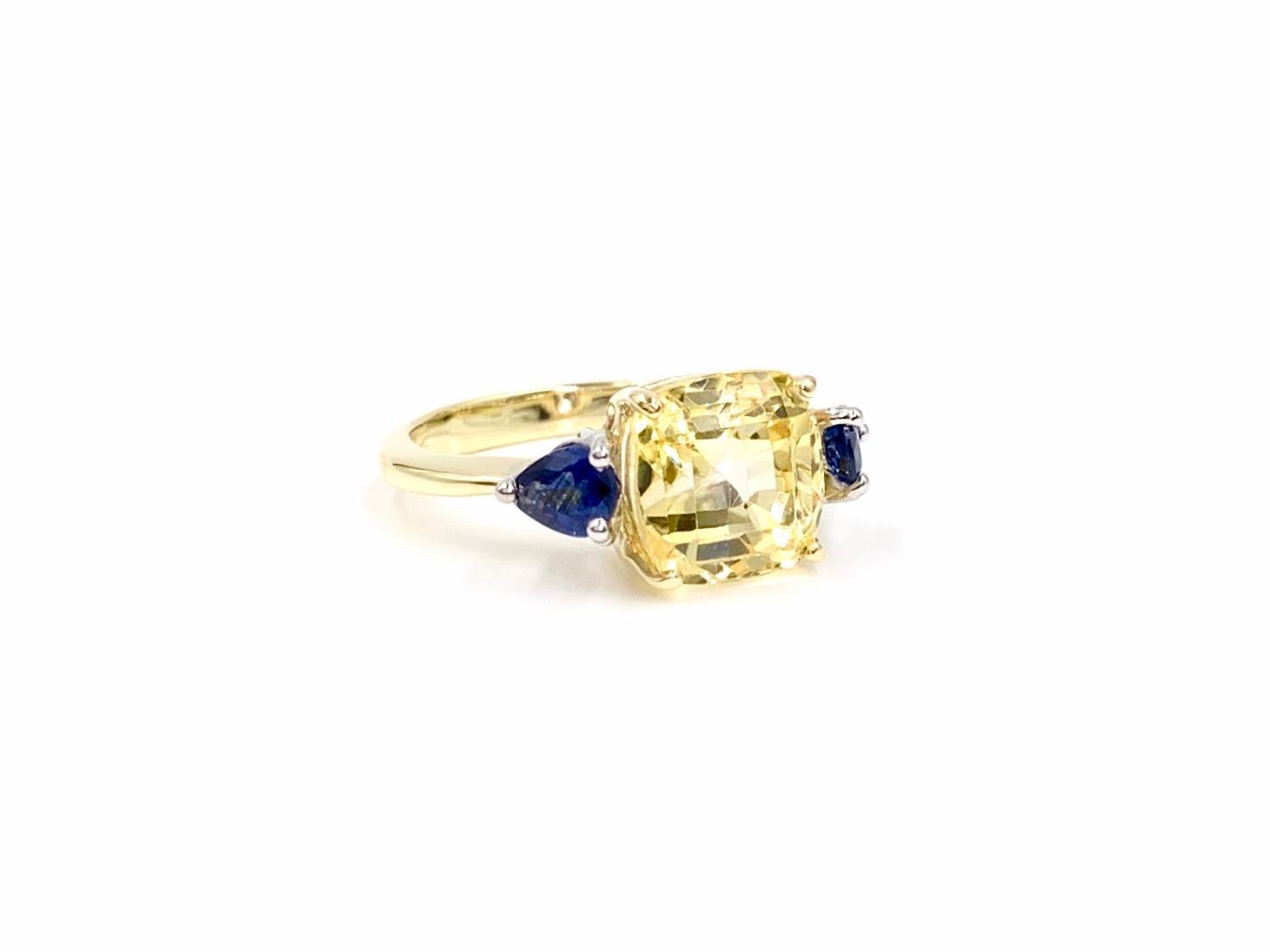 A beautiful 14 karat two tone three stone style mounting features a well saturated and vibrant 7.88 carat cushion cut yellow sapphire resting between two pear shape blue sapphires at .81 carats total weight. Blue sapphires are set in individual