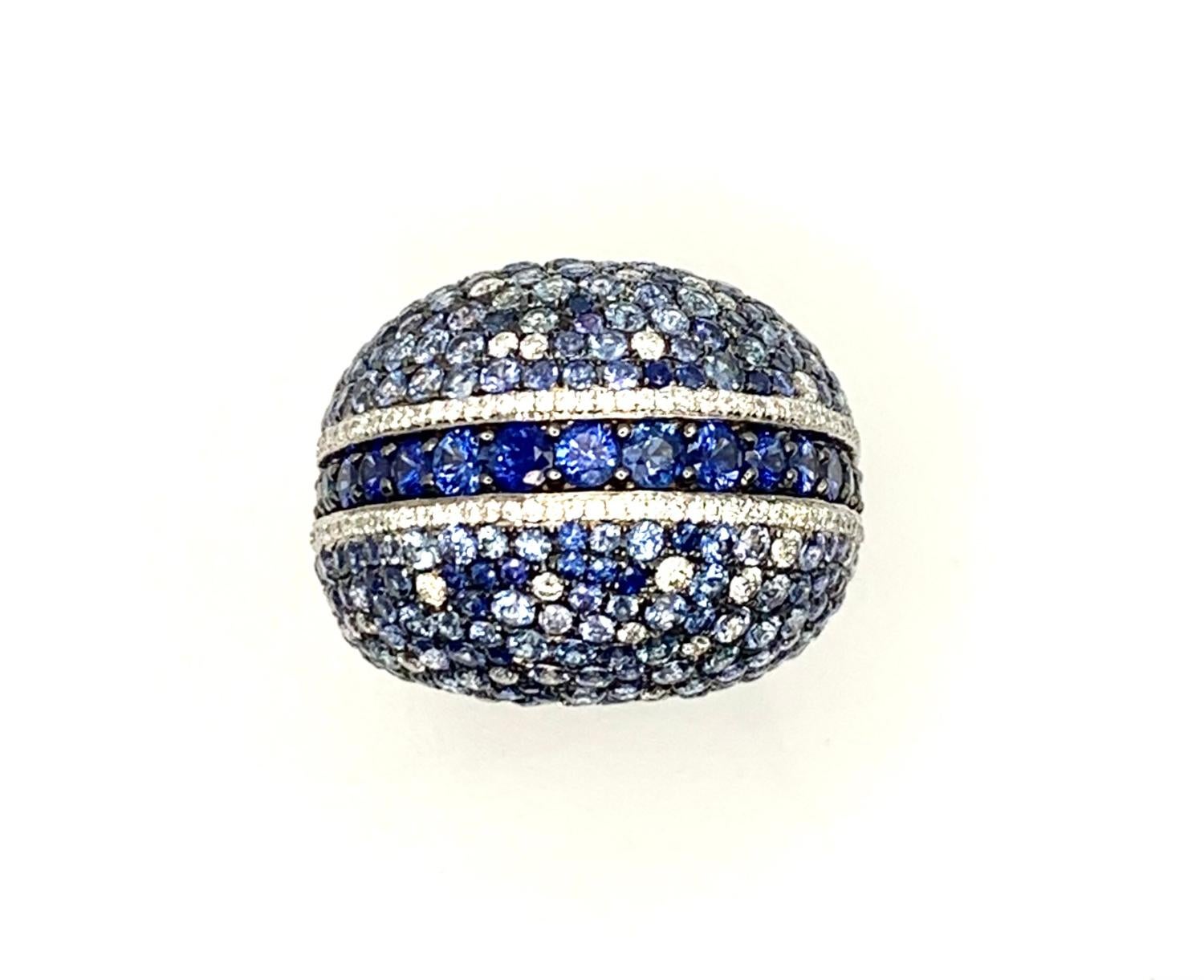 This large and impressive dome ring features sparkling shades of blue sapphires that have been pave set in 18k white gold with brilliant cut diamonds! A bold line of rich, blue sapphires forms the central row of this ring, highlighted on both sides