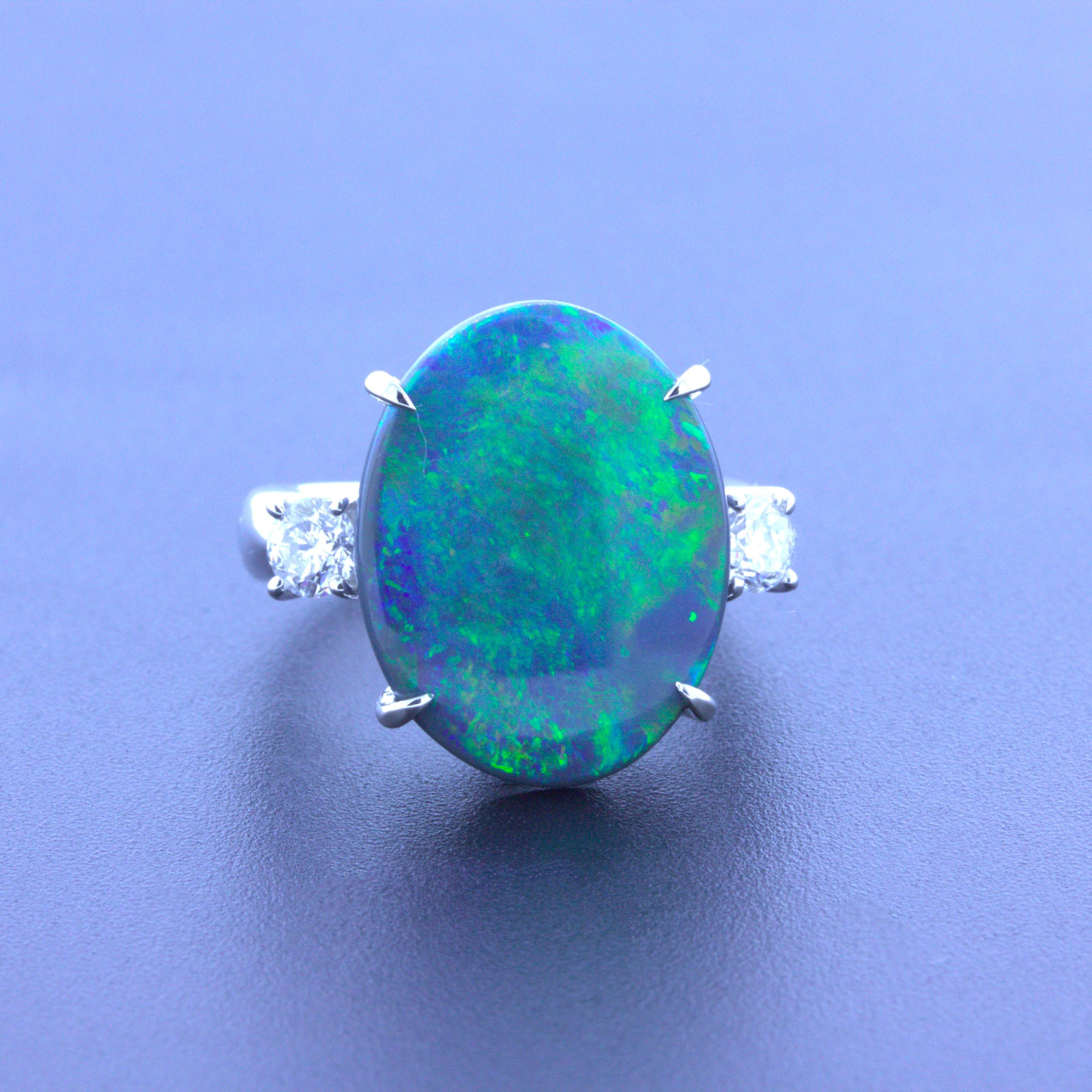 A classic 3-stone ring featuring a natural Australian black opal. It weighs 7.92 carats and has beautiful play-of-color as flashes of green, blue, yellow, and orange all dance across the stone as it is moved across the light. It is complemented by 2