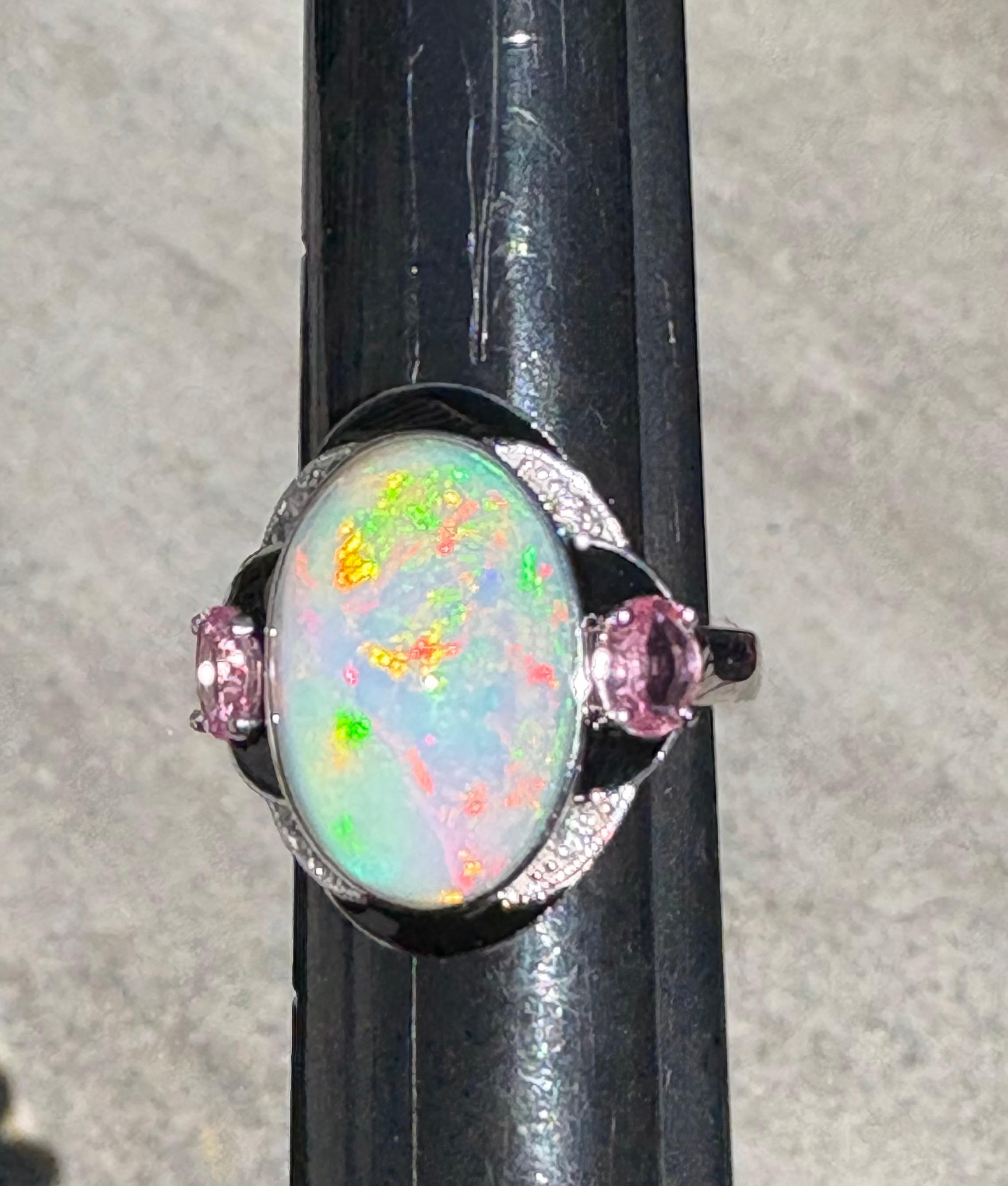 This exquisite ring features a 7.96-carat, oval-cut opal that radiates an exceptional fire. The centerpiece is flanked on the east and west by two 0.71-carat pink sapphires, and the design is further elevated by delicate 0.04-carat diamond accents