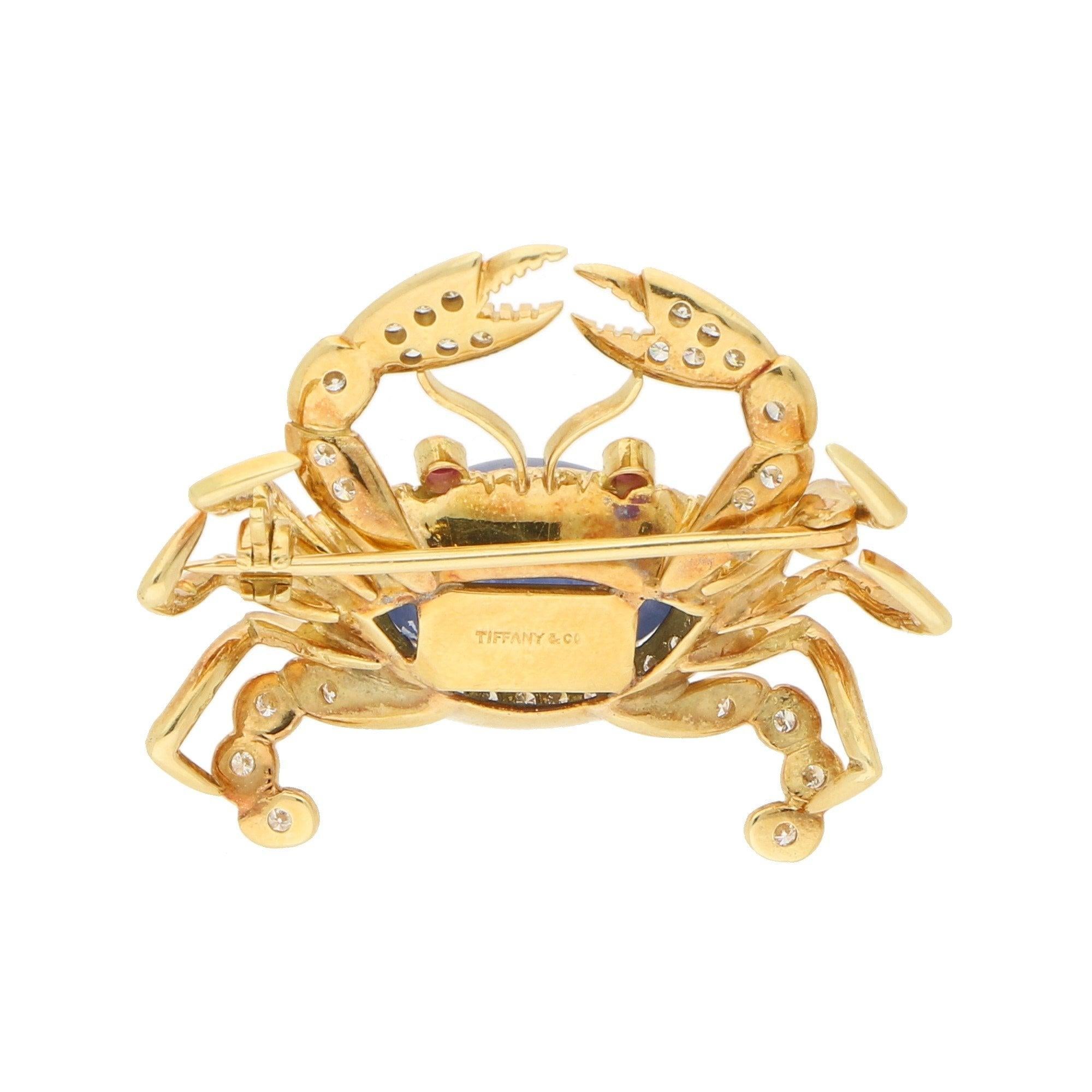 A Tiffany & Co. sapphire, diamond and ruby crab pin brooch in 18-karat yellow gold, circa 1990. The crab's body is designed with a cabochon sapphire amidst a sea of pave-set round brilliant-cut diamonds, the claws and swimming legs similarly-set