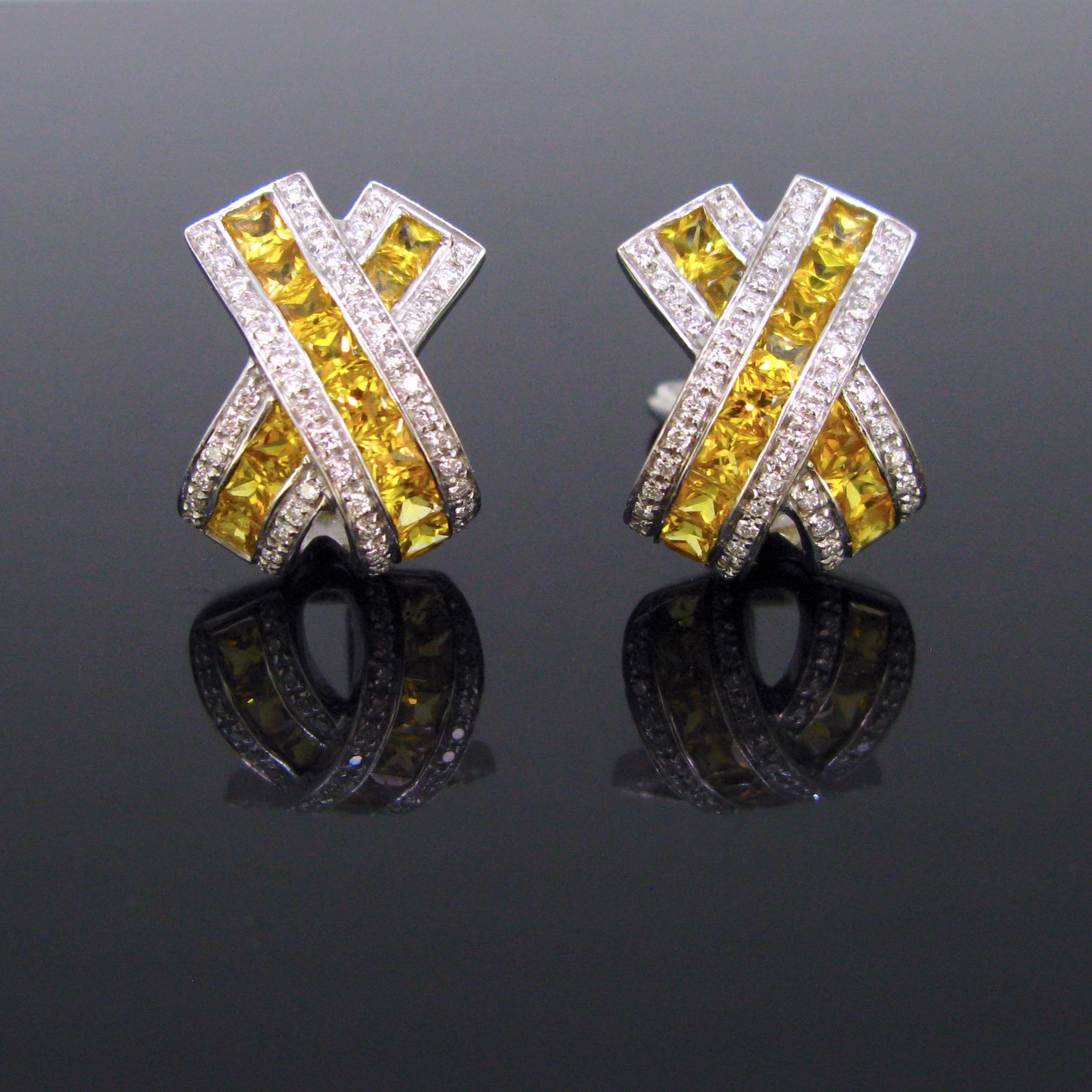 This pair of earrings has a nice X shape design. It is set with French cut yellow sapphires shouldered with brilliant cut diamonds. There is an approximate total carat weight of 7ct of sapphires. The earrings are made in 18kt white gold. They are in