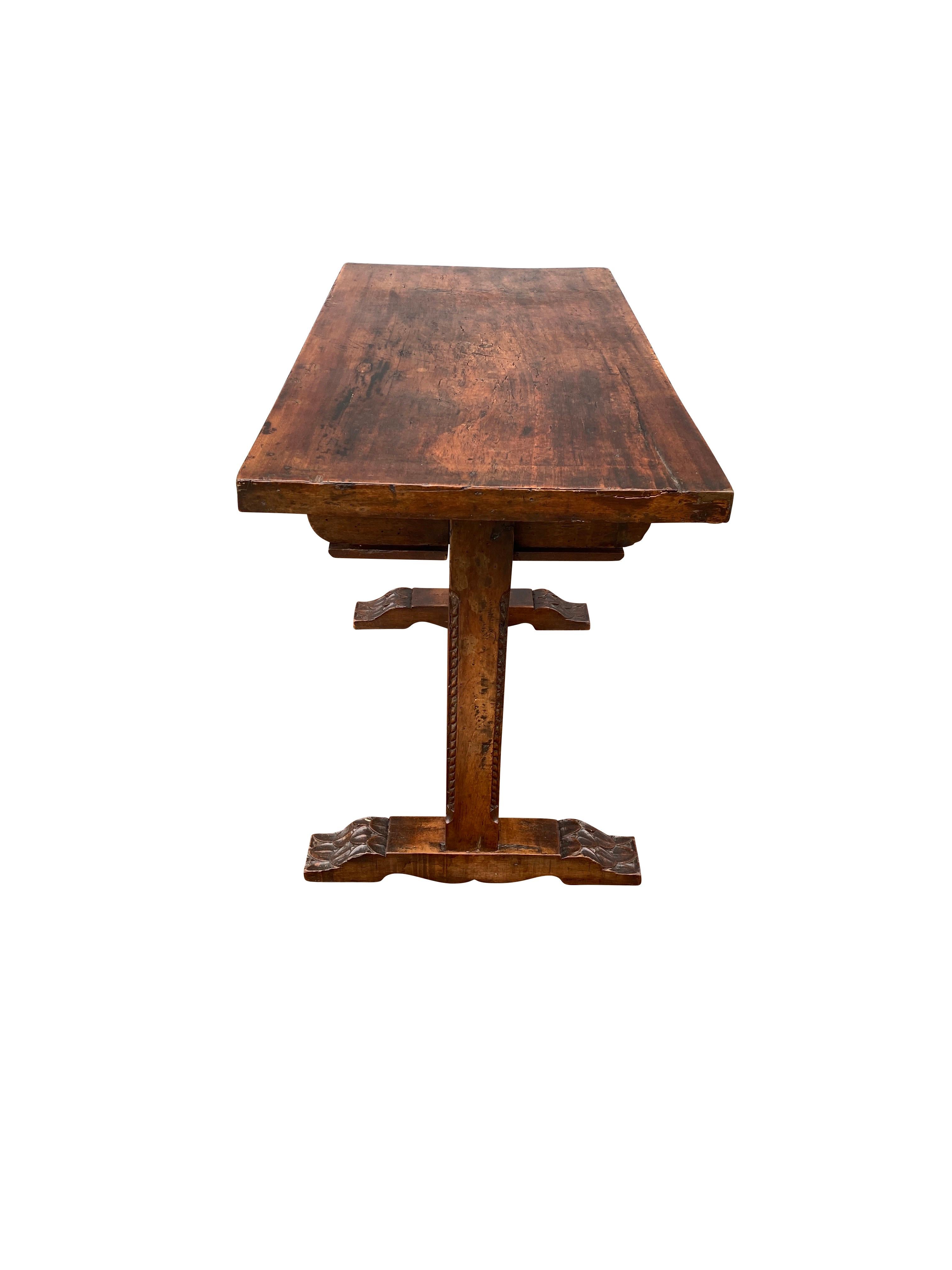 Small table with rectangular top over two carved drawers, square trestle supports, stretcher and flat carved feet.