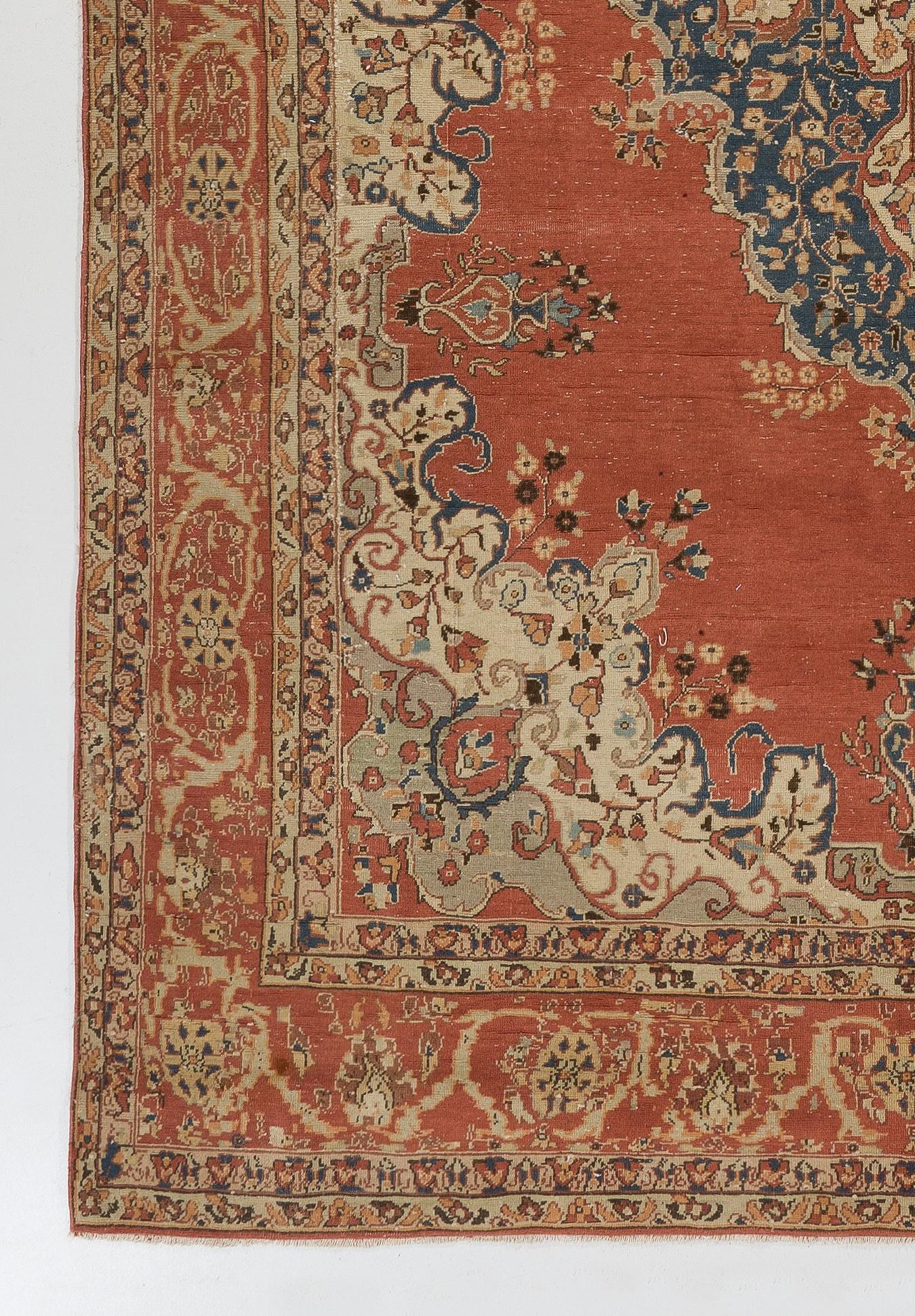 This vintage hand knotted Turkish rug features an elegant, classical medallion in dark indigo adorned with dainty floral motifs and scrolling vines against a vibrant, plain field in madder red, surrounded by curvilinear, floral corner pieces in