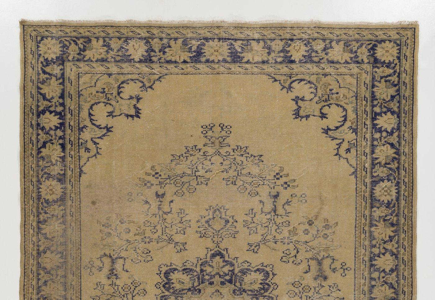 A vintage hand-knotted Turkish Oushak rug from the 1960s with distressed low wool pile on cotton foundation. It features a central medallion in indigo blue against a golden sand colored background decorated with scrolling leafy vines as well as a