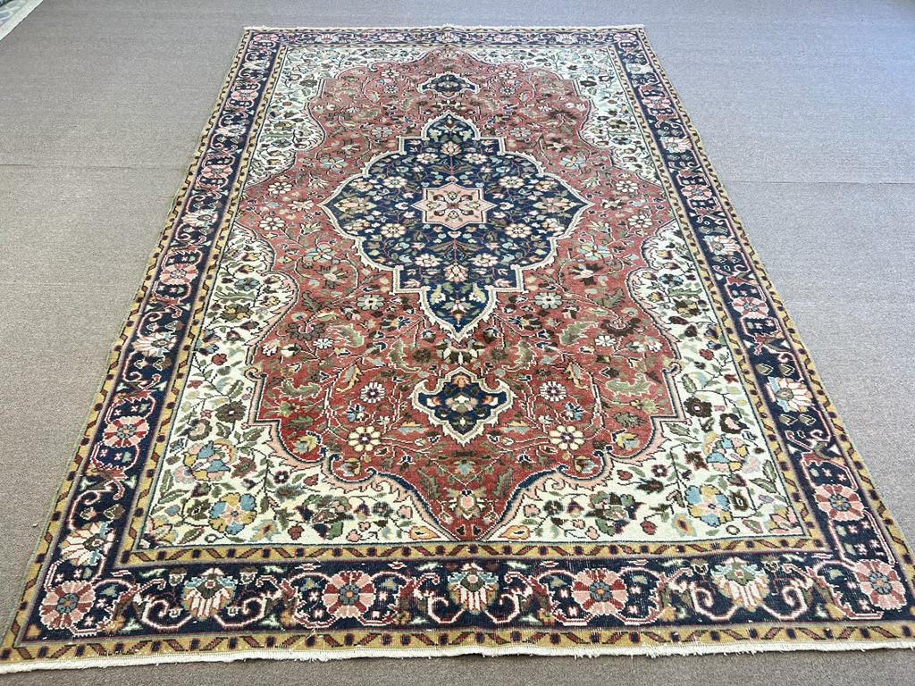 This room-size vintage hand knotted Turkish rug boasts a central medallion in navy blue against a key-hole shaped field in red and curvilinear corner-pieces in ivory surrounded by two guard strips and a main border in between. Every inch of every