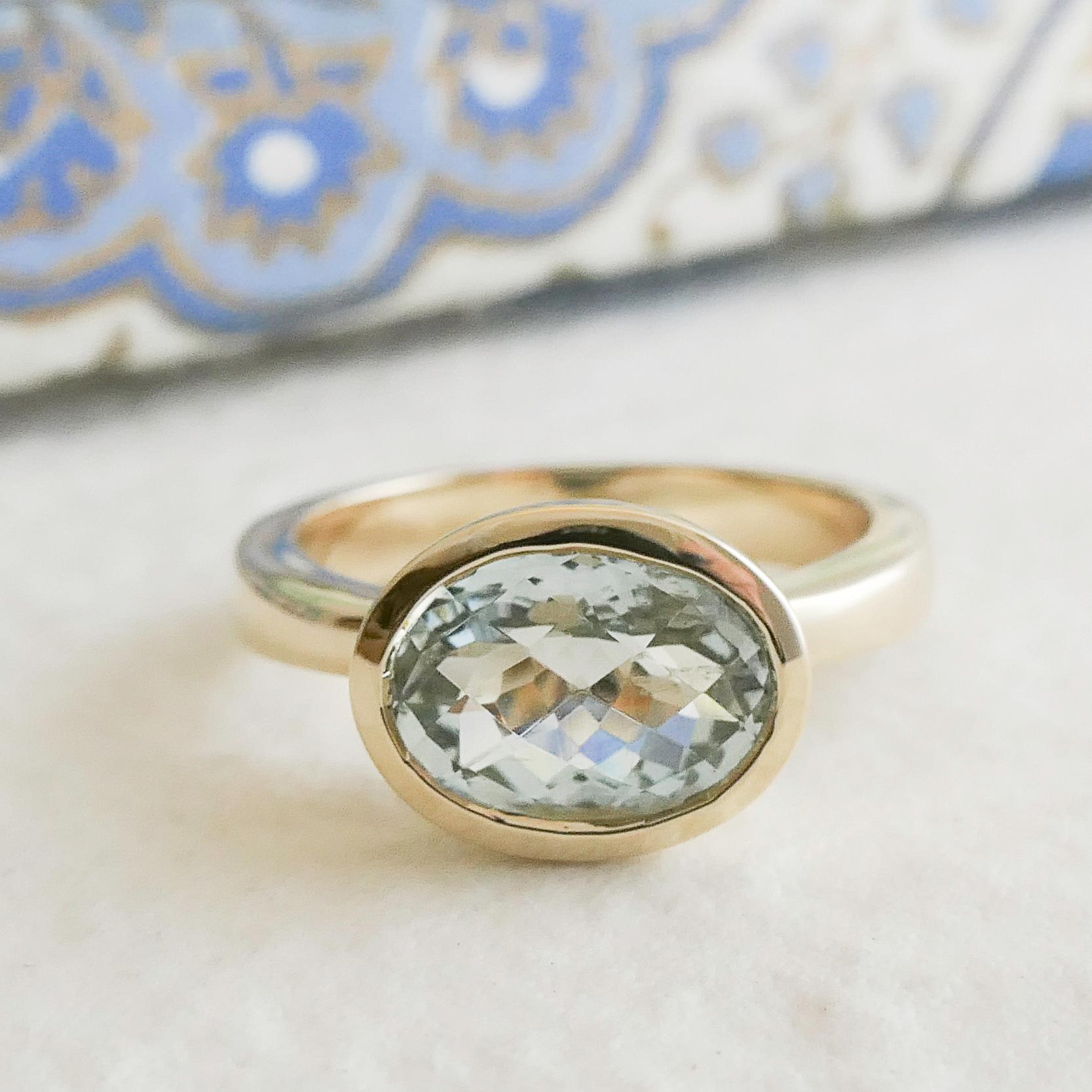 Cette élégante bague est ornée d'une aigue-marine ovale à facettes de 7x10 mm, sertie dans un élégant chaton en or jaune 14 carats. La teinte bleue pâle et douce de l'aigue-marine contraste magnifiquement avec les tons chauds et dorés, créant un