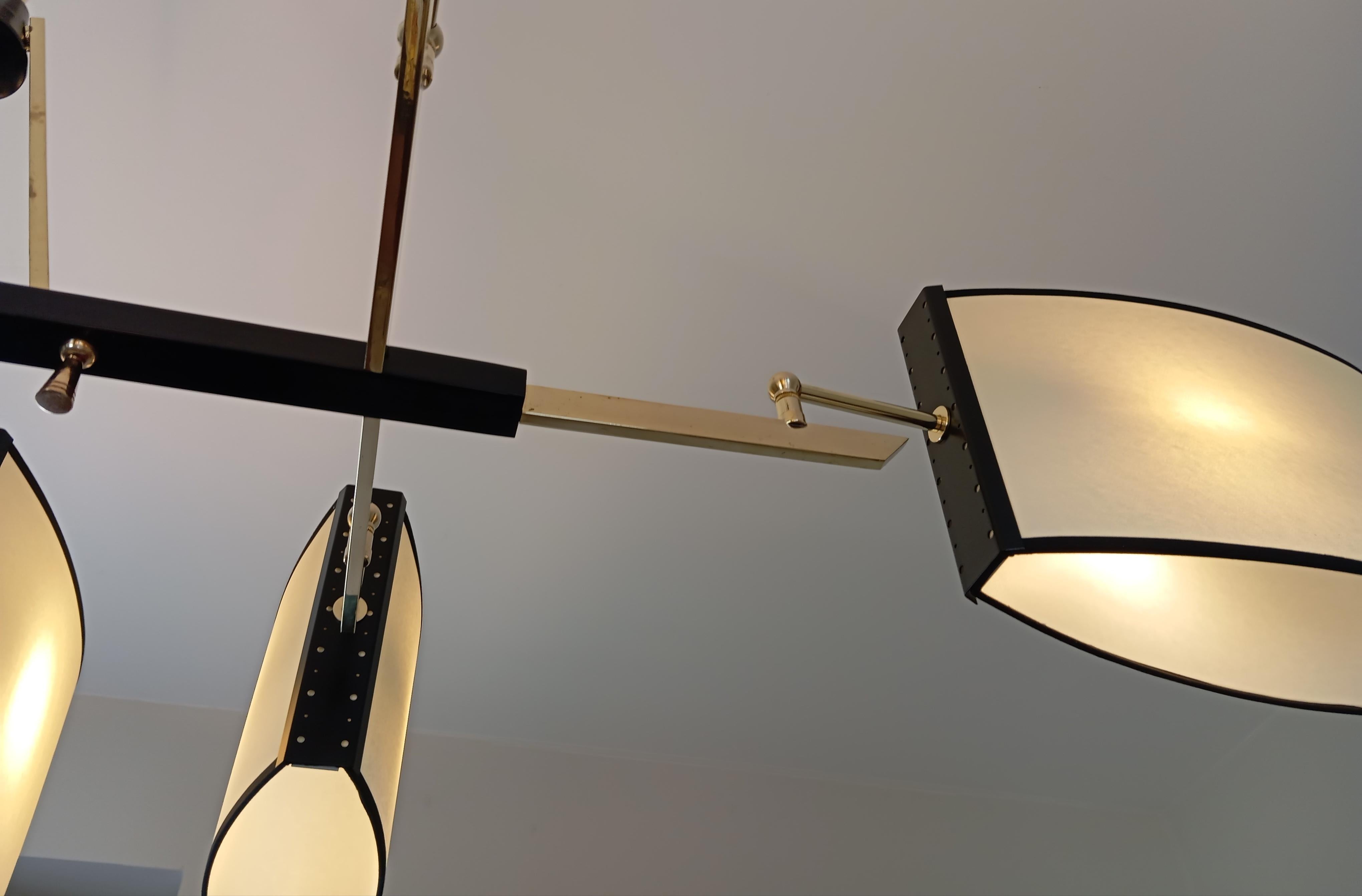Lampadario in metallo e ottone, composto da una base rettangolare in metallo laccato nero, su cui sono fissati 8 bracci luminosi in ottone, che sostengono paralumi di forma ovale.
Opera francese del 1950 circa, attribuita alla Maison Lunel.
Il