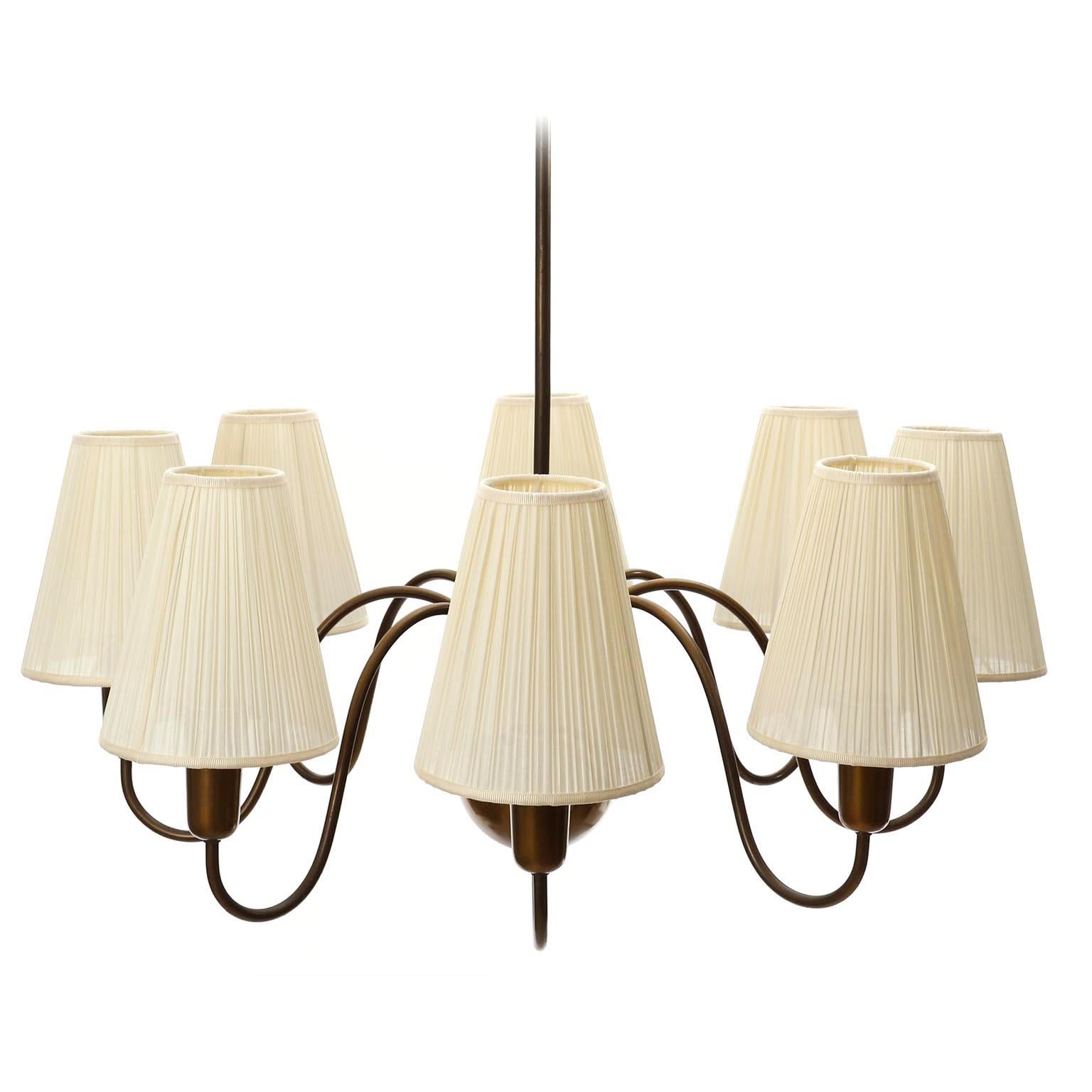 A fantastic eight-arm pendant chandelier made of patinated brass (bronze finish) with organically curved arms and cream colored pleated fabric shades, manufactured in Austria circa 1950.
The brass parts have lovely patina and a warm aged hue. The