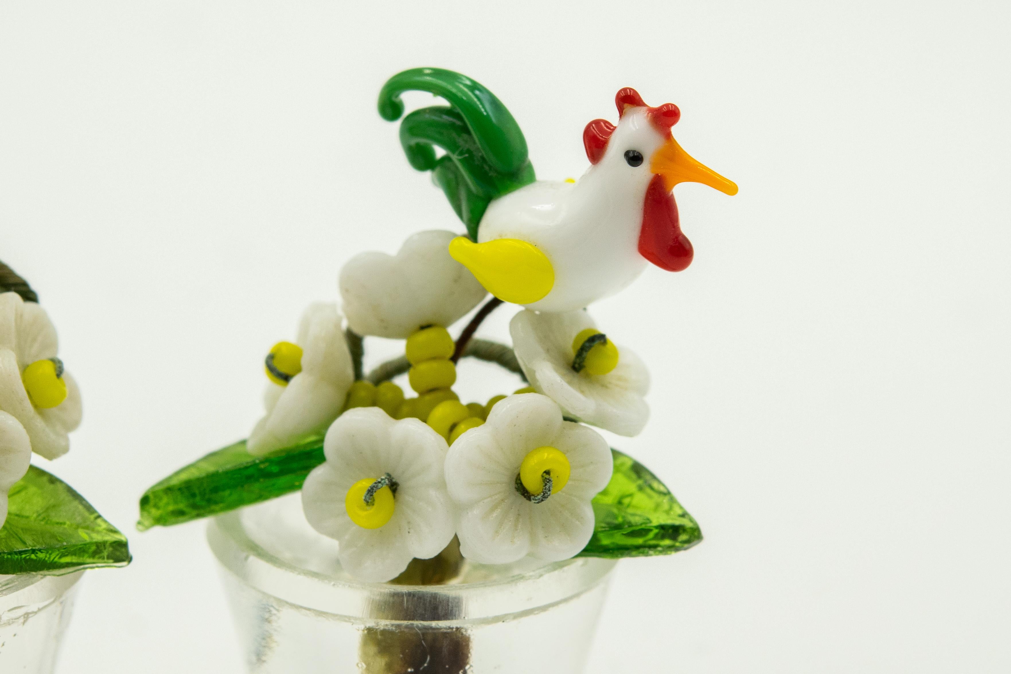 Set of 8 Czech glass place card holders in original box

Each clear glass flowerpot has 5 glass flowers on yellow glass bead stems, 2 glass leaves and a bird.
The tiny bouquets are wired together and there is thicker double loop wire for the