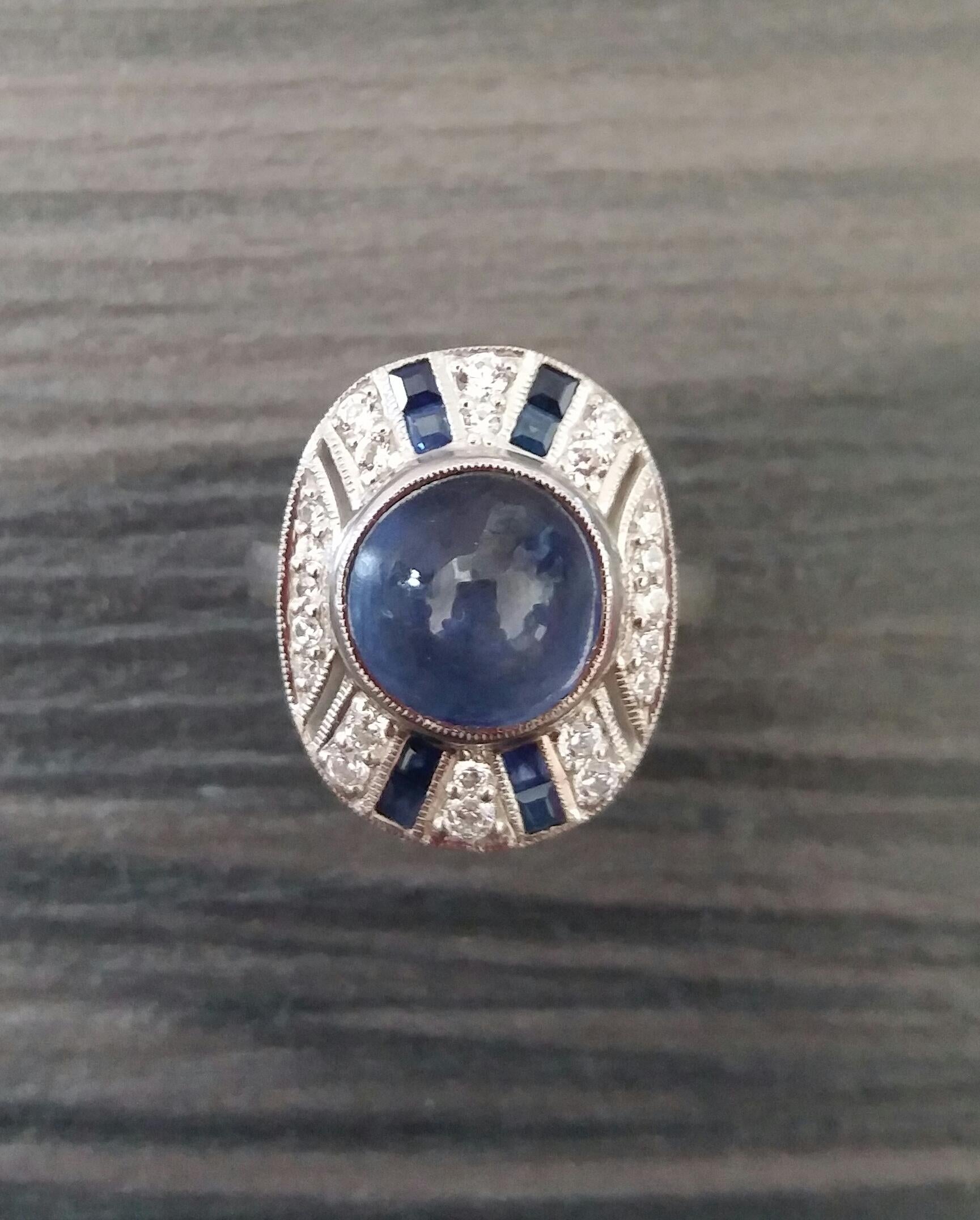 Classy Art Deco 14 White Gold Ring with a 8 Carats Round Blue Sapphire Cabochon in the center 4 small lines of rectangular cut Blue Sapphires with 