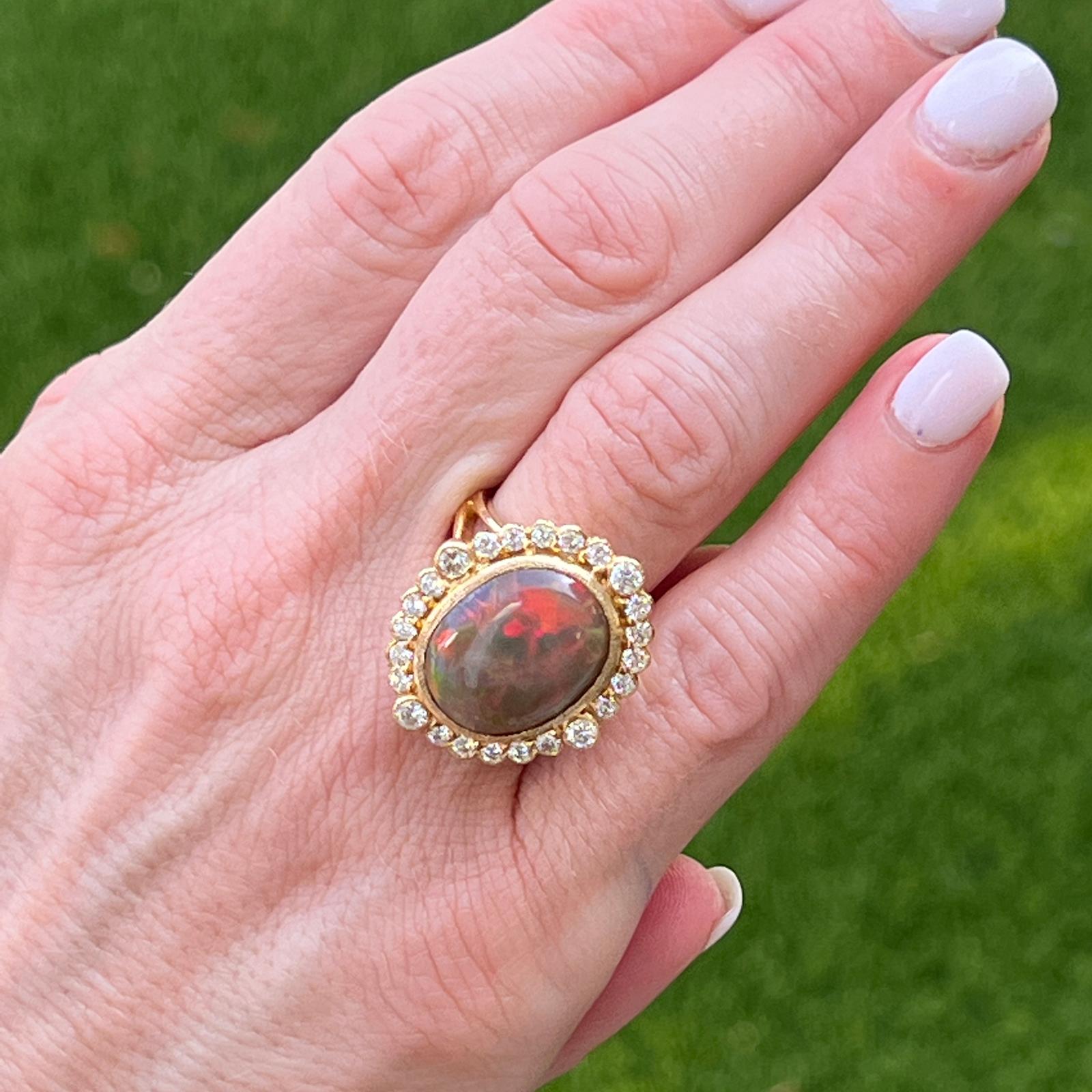 Beautiful opal diamond cocktail ring fashioned in 18 karat yellow gold. The cabochon cut fiery opal weighs approximately 8 carats and features sparkles of orange, green, and blue hues. The opal is surrounded by 24 round brilliant cut diamonds