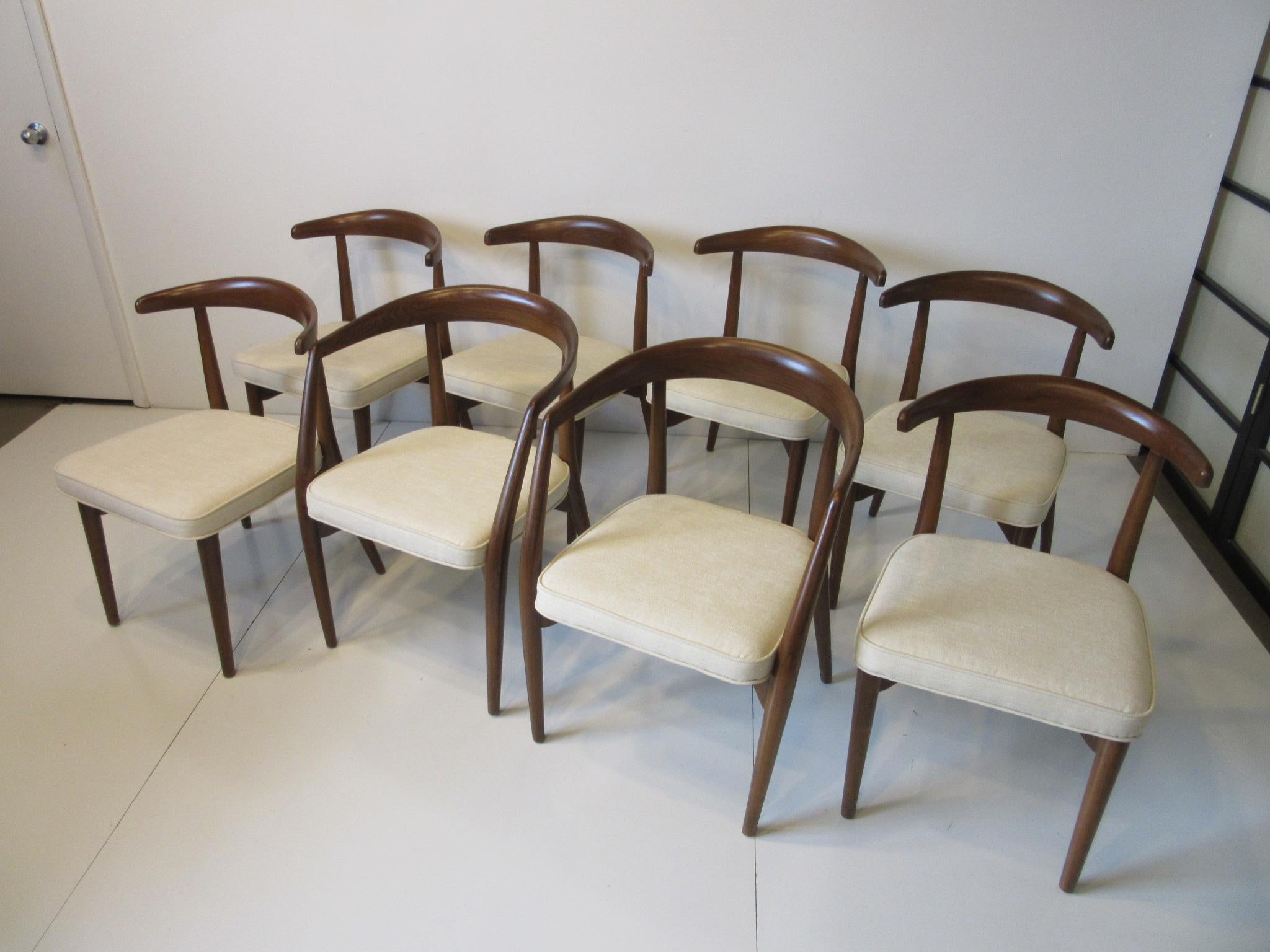 A set of eight sculptural dining chairs in a dark walnut finish with two Armchairs and six side chairs all with newly upholstered seats in a cream colored linen styled contract fabric . These handsome and well crafted chairs would work with any type