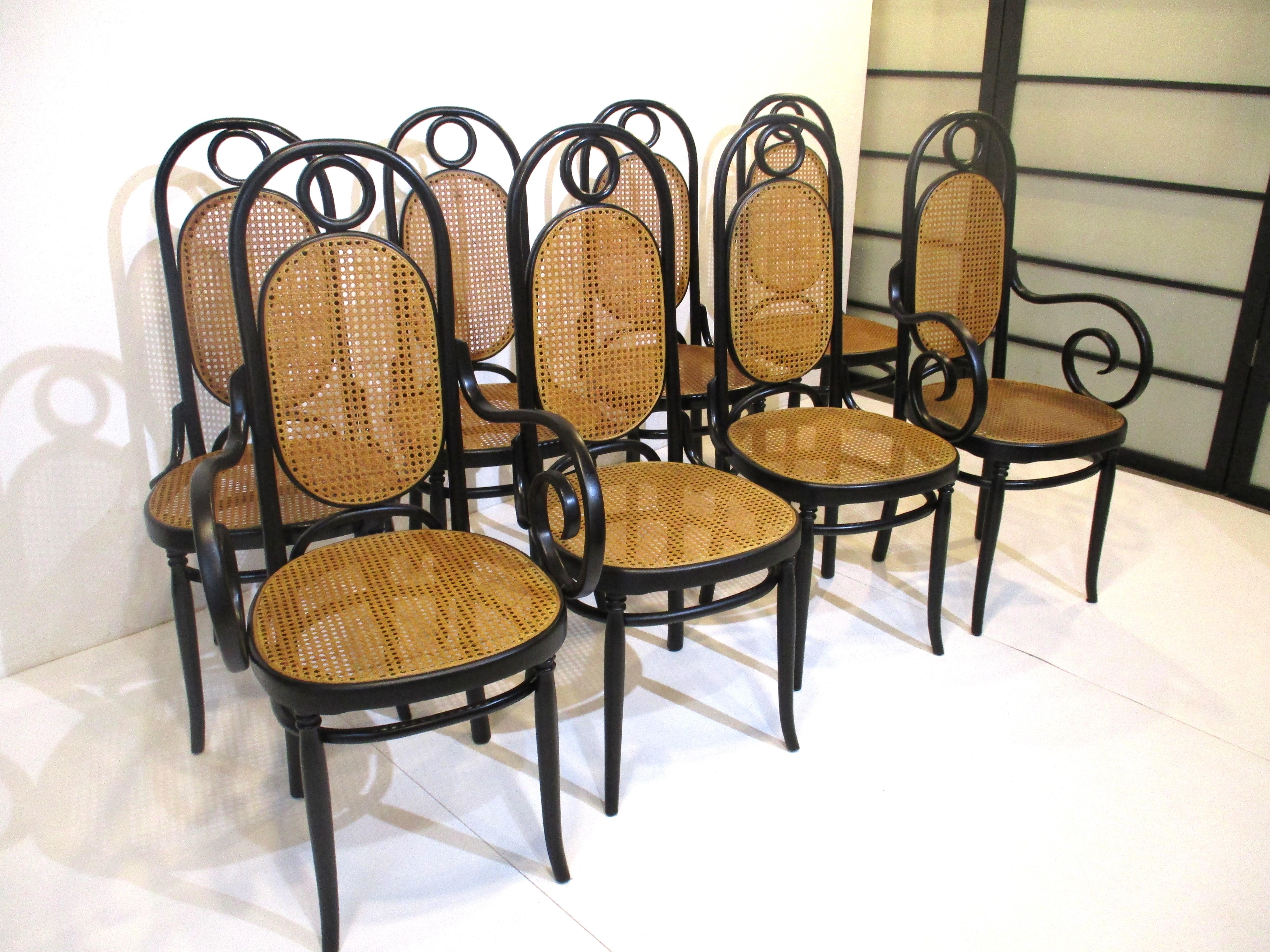 A set of eight high back sculptural satin black bentwood dining chairs with woven back and bottom cane seats . The set contains two arm or head chairs and six side chairs manufactured by the Thonet chair company made in Italy . A classic styled
